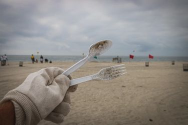 Gloved hand holding a plastic spoon and fork at a beach during a coastal clean-up