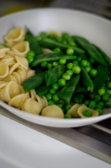 Plate filled with blanched English peas, Romano beans and orecchiette pasta