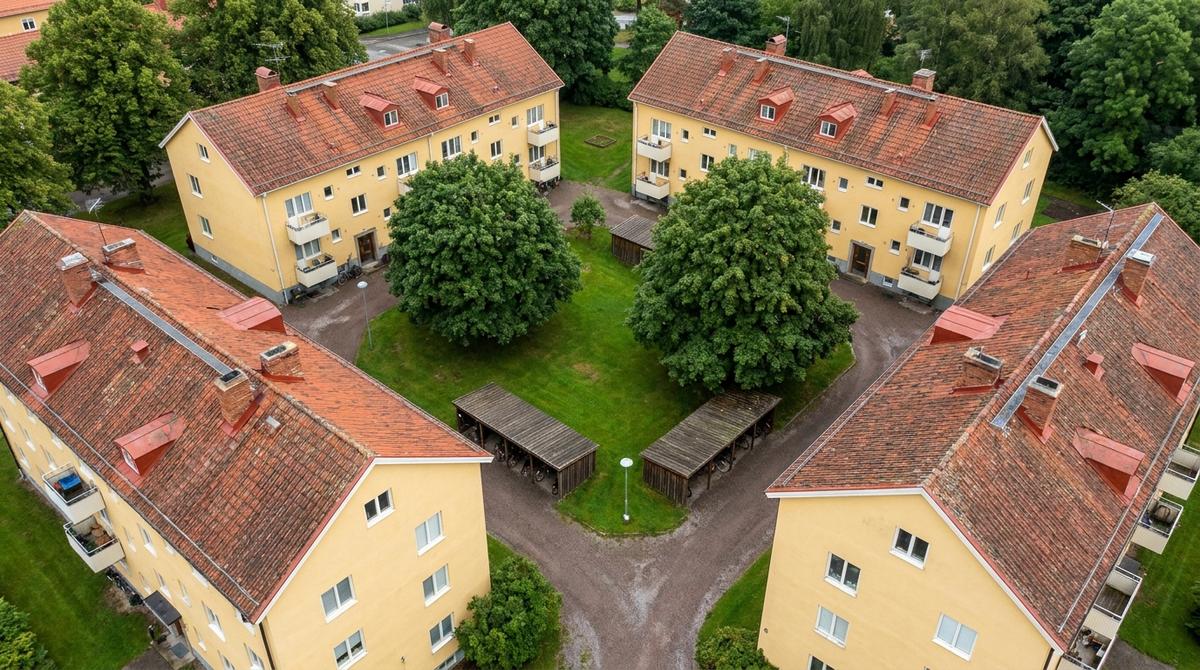 Flygbild av en grupp gulputsade flerbostadshus i tre våningar med röda tegeltak kring en grön gård med stora träd och cykelskjul