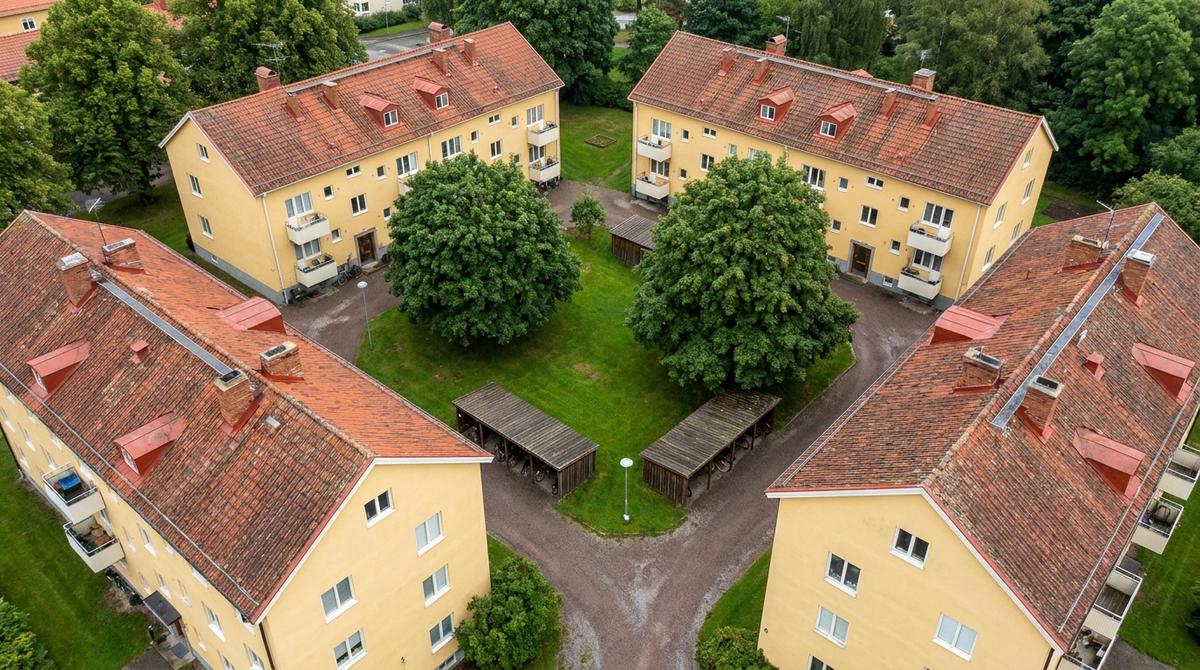 Flygbild av en grupp gulputsade flerbostadshus i tre våningar med röda tegeltak kring en grön gård med stora träd och cykelskjul