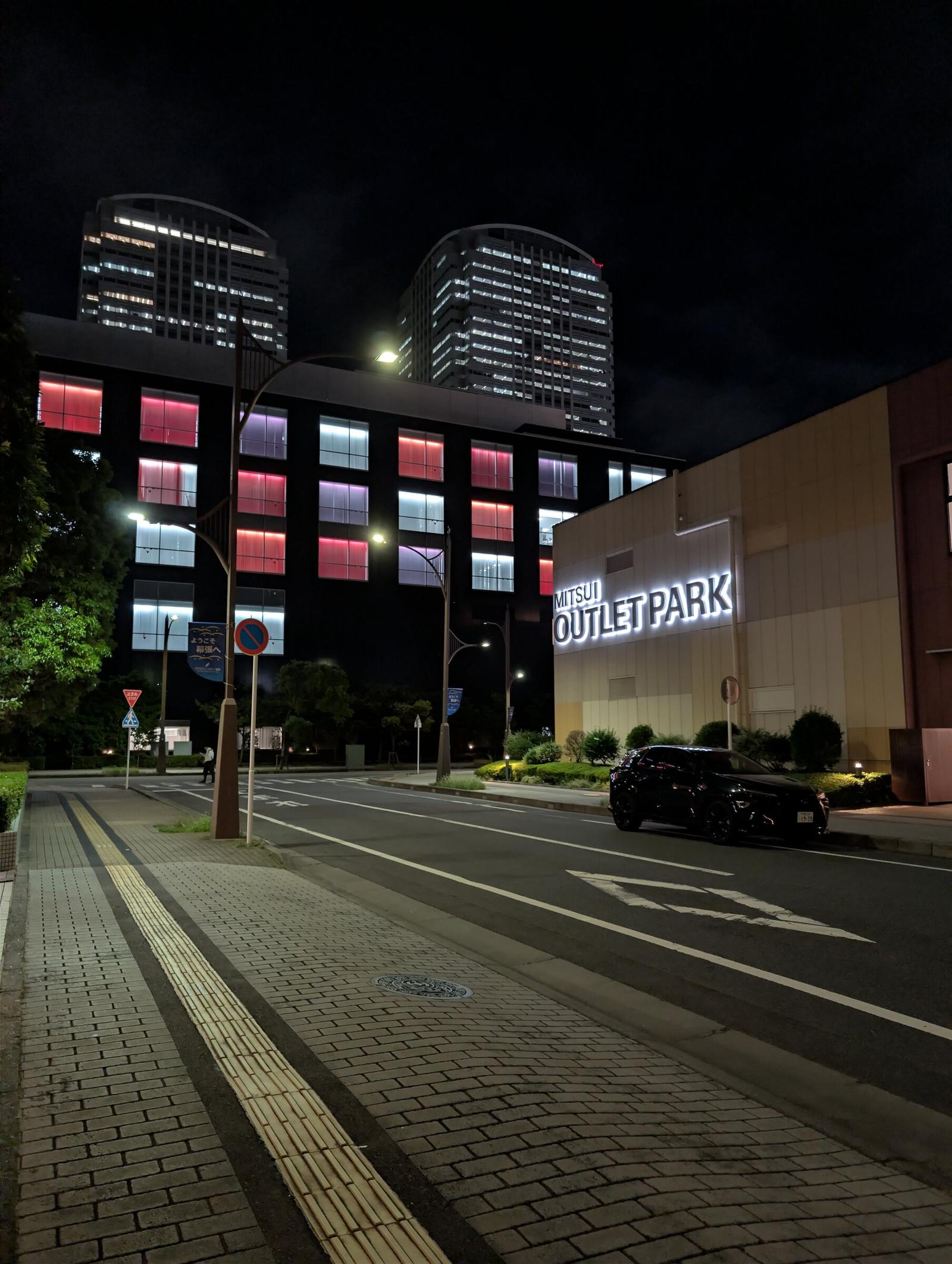 Gata i Makuhari på kvällen med upplysta höghus och skylten för Mitsui Outlet Park.
