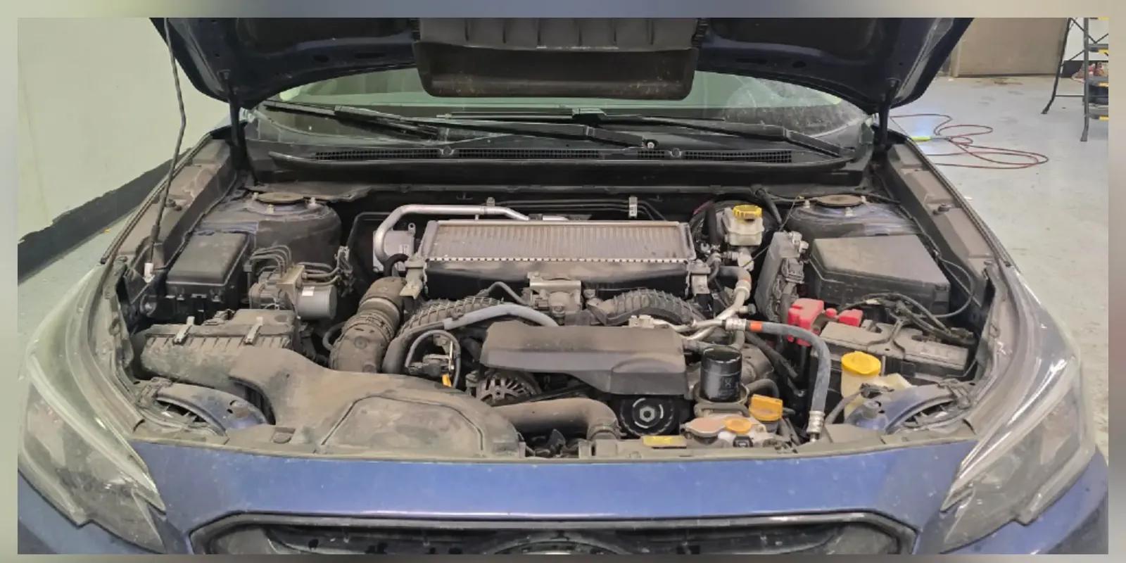 Subaru engine bay coated in dust and road film before cleaning in Anchorage, Alaska