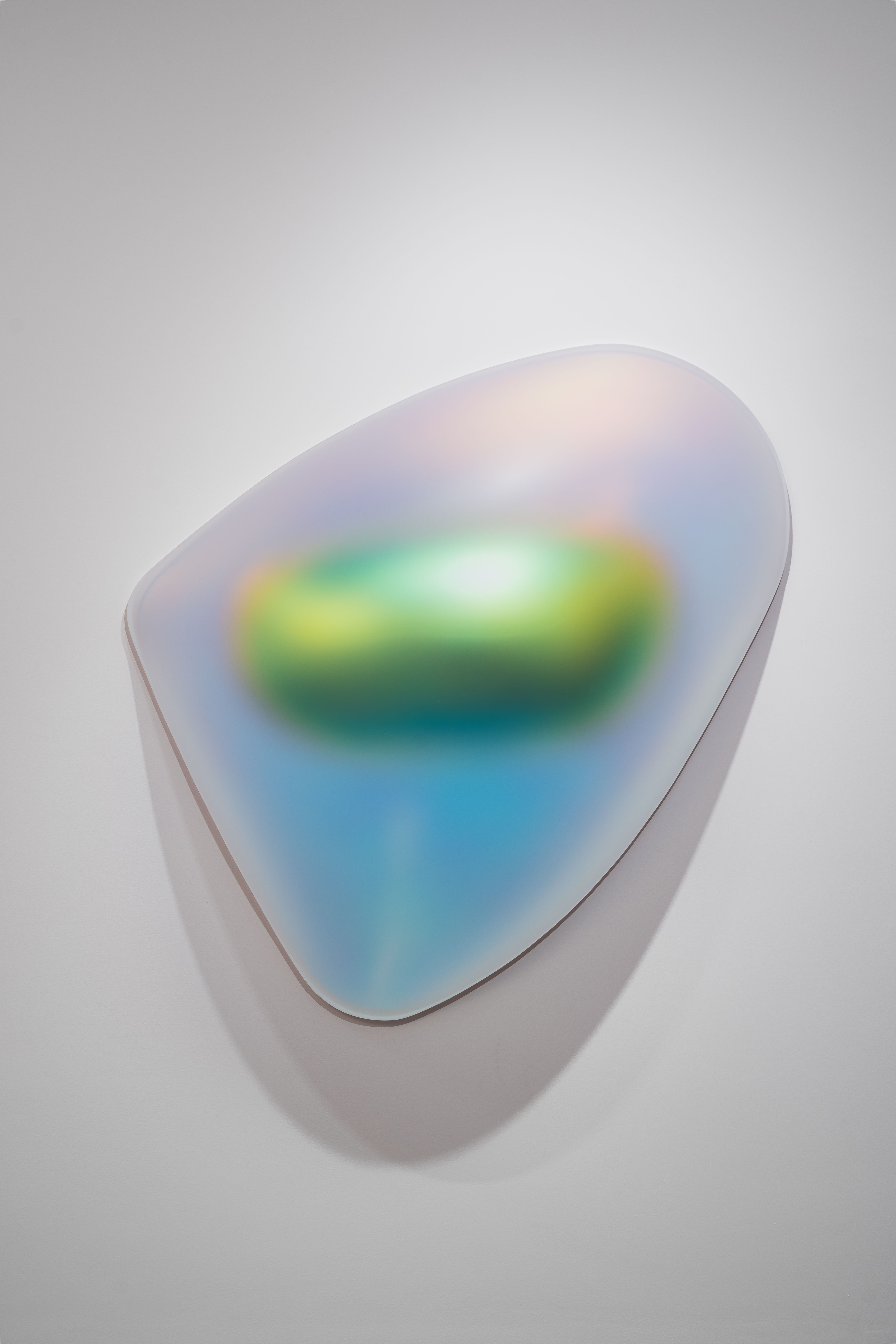 An irregularly shaped wall sculpture with a smooth, semi-translucent surface. The form glows in gradient hues of blue, green, pink, and gold, creating a fluid, futuristic impression reminiscent of a light-diffusing organic object.
