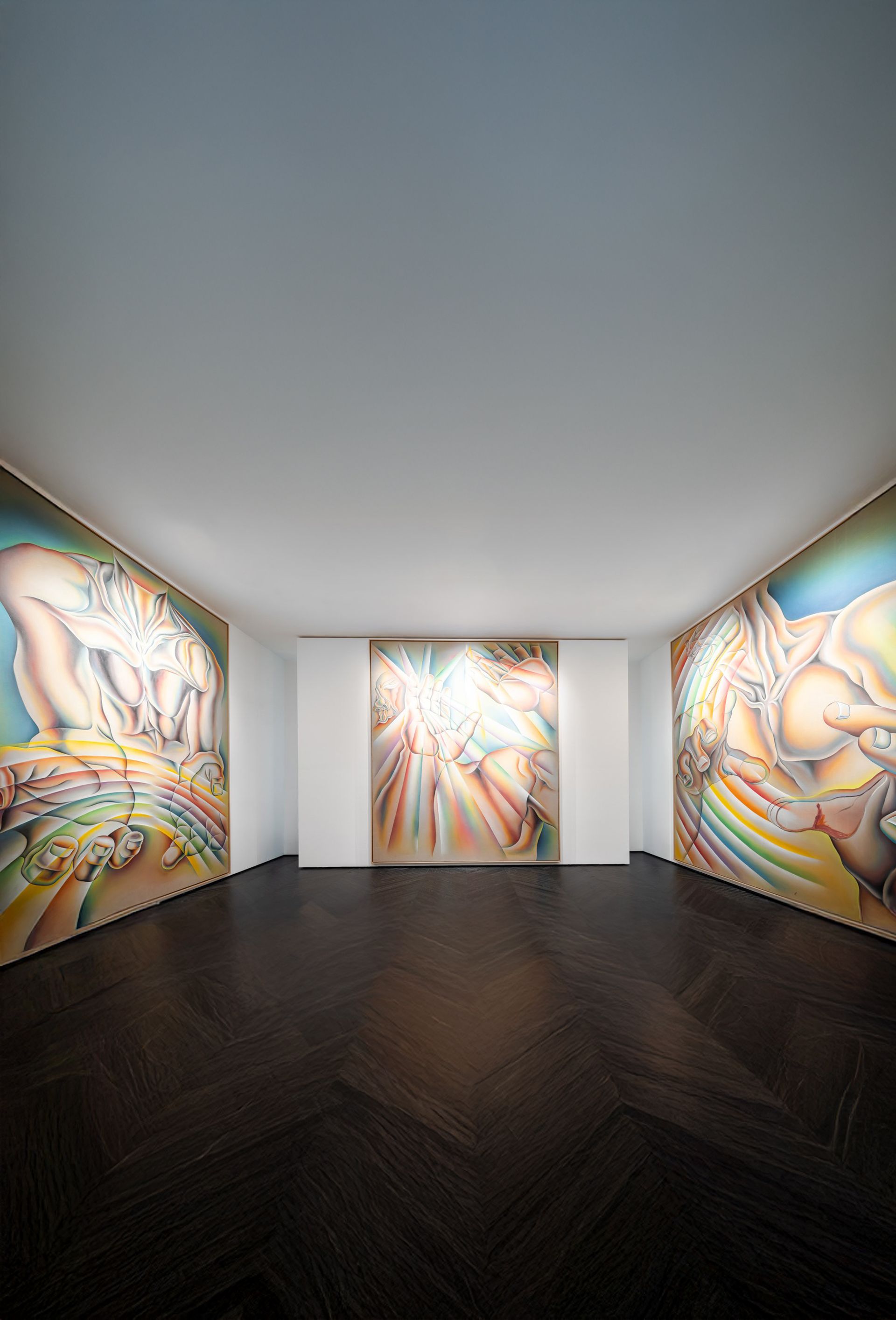 A large, colorful painting depicting a stylized, muscular torso without a head, with outstretched hands in the foreground. The figure’s body and hands are rendered in smooth, flowing gradients of pink, blue, yellow, and green, creating a luminous, almost iridescent effect. The curved forms and layered colors evoke movement and energy. The artwork is framed in light wood and displayed on a white gallery wall.