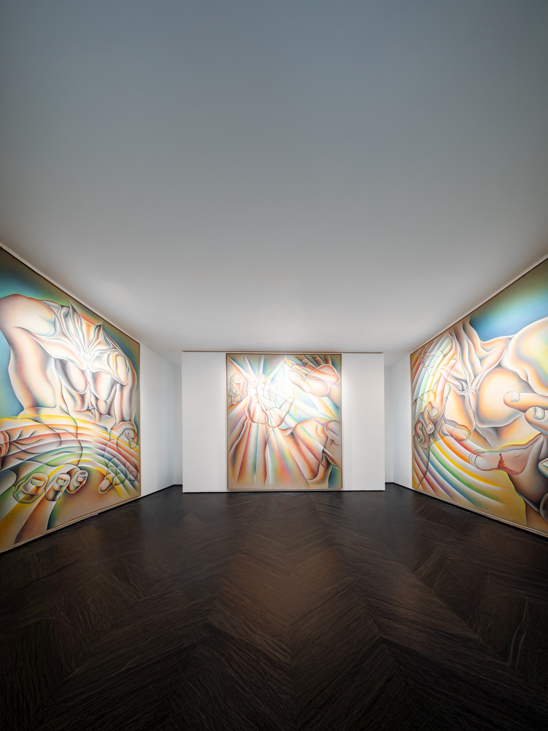 A large, colorful painting depicting a stylized, muscular torso without a head, with outstretched hands in the foreground. The figure’s body and hands are rendered in smooth, flowing gradients of pink, blue, yellow, and green, creating a luminous, almost iridescent effect. The curved forms and layered colors evoke movement and energy. The artwork is framed in light wood and displayed on a white gallery wall.