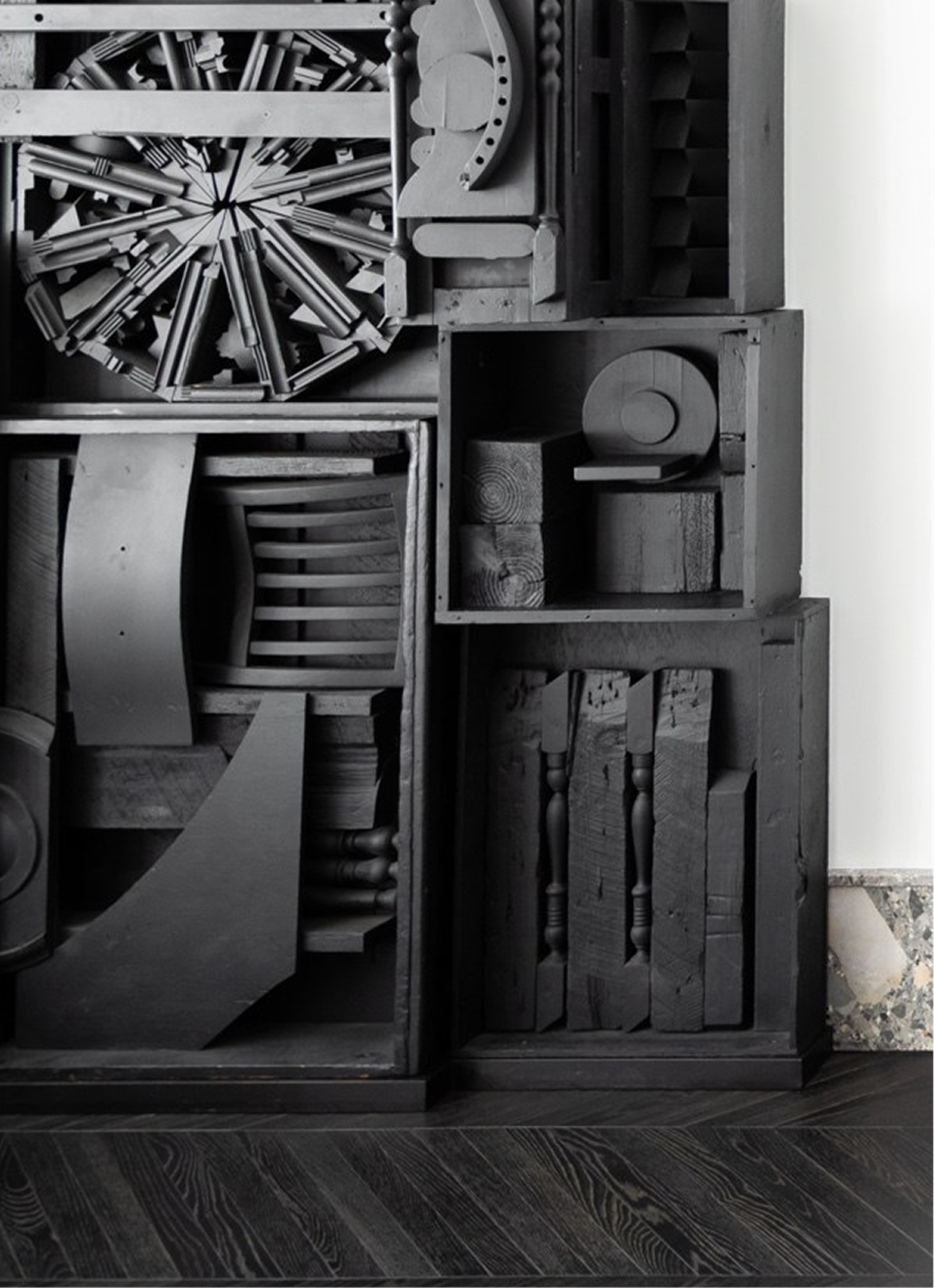Black matte shapes compose a sculpture on synthetic hardwood flooring.