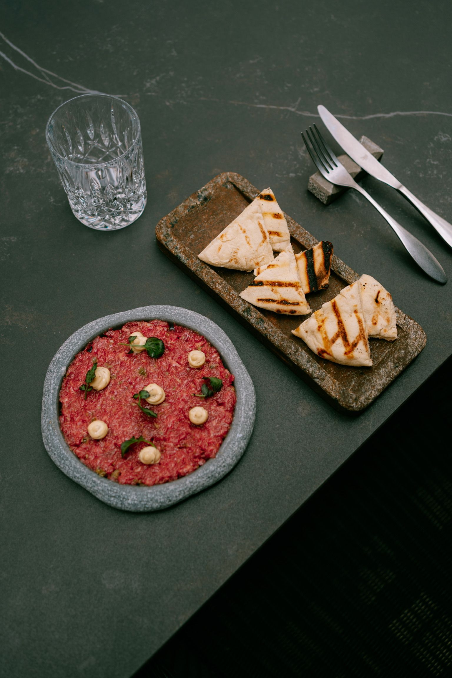 Steak tartare on a stone plate with grilled flatbread on a dark table