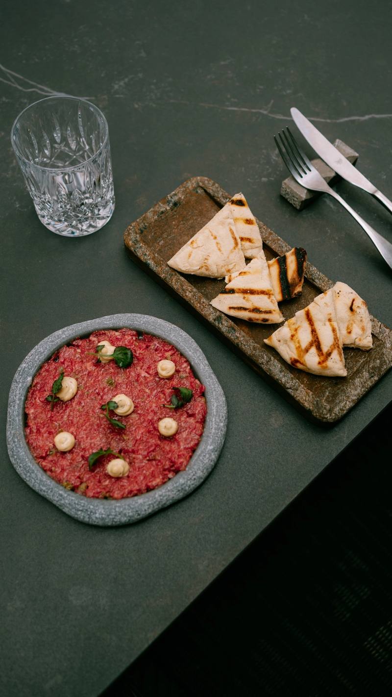 Steak tartare on a stone plate with grilled flatbread on a dark table