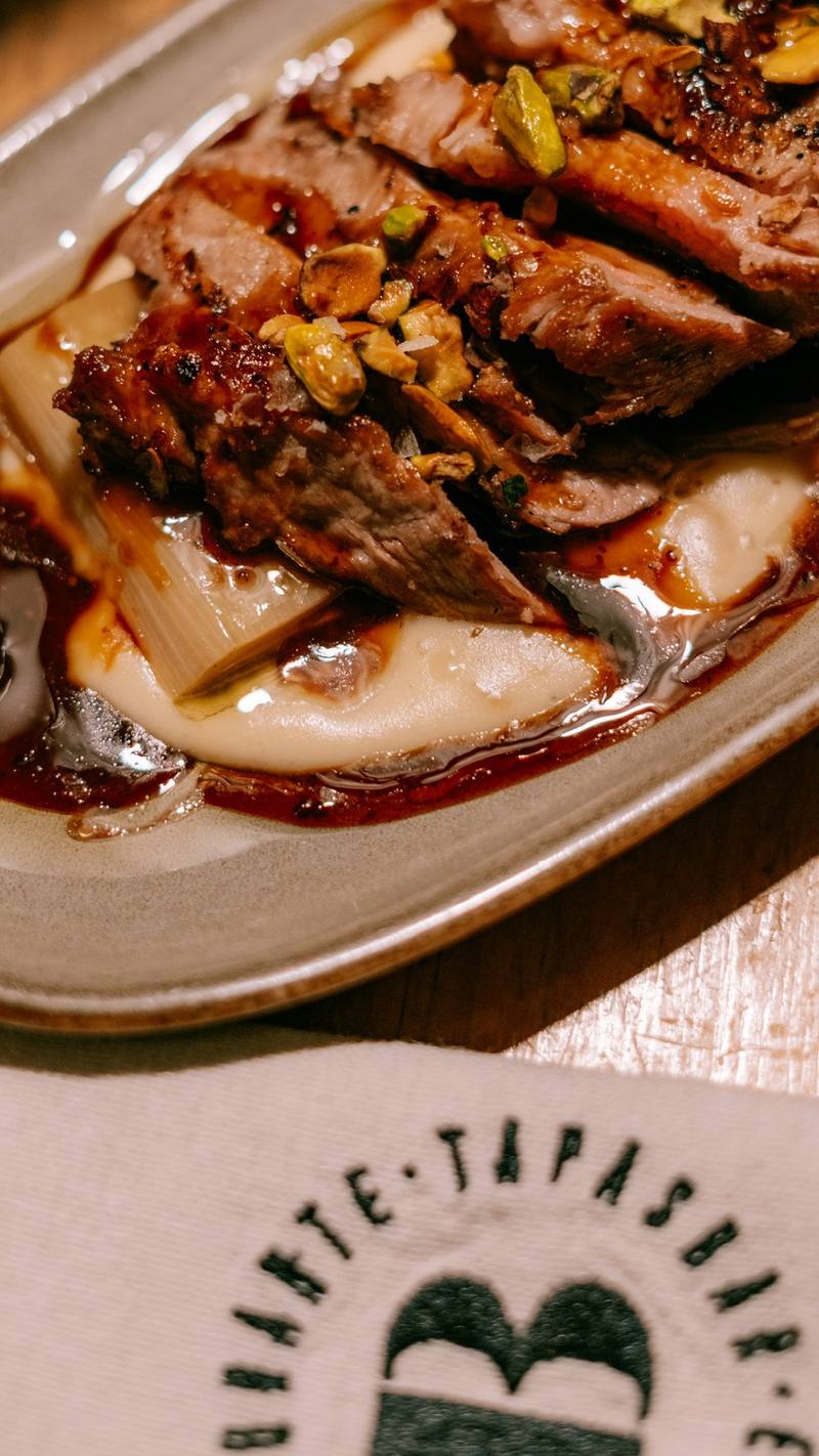 Carne a la brasa en lonchas con pistachos sobre puré cremoso