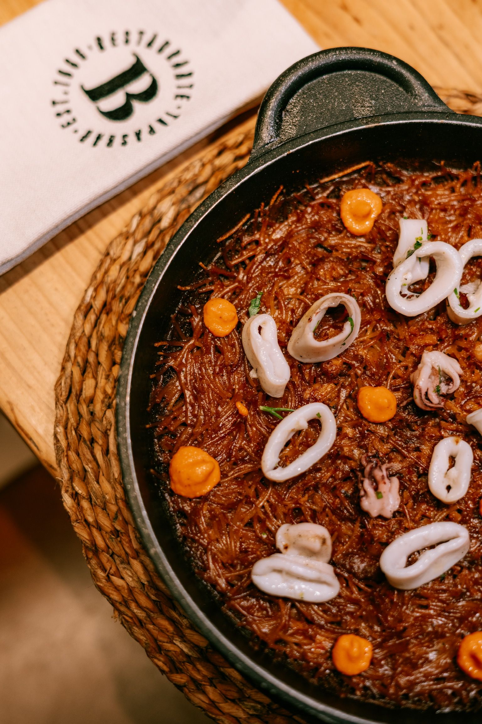 Fideos tostados con calamares y puntos de alioli en una sartén de hierro