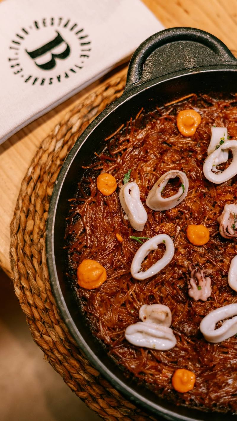 Fideos tostados con calamares y puntos de alioli en una sartén de hierro