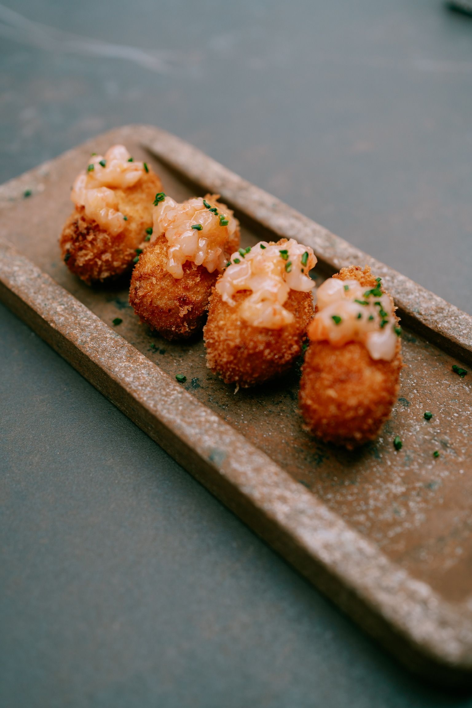 Four croquettes topped with prawn tartare on an earthenware dish