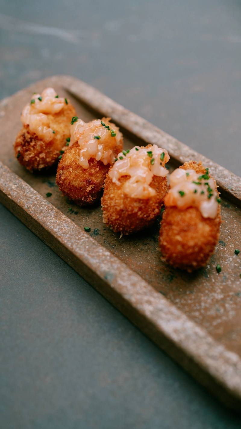 Four croquettes topped with prawn tartare on an earthenware dish
