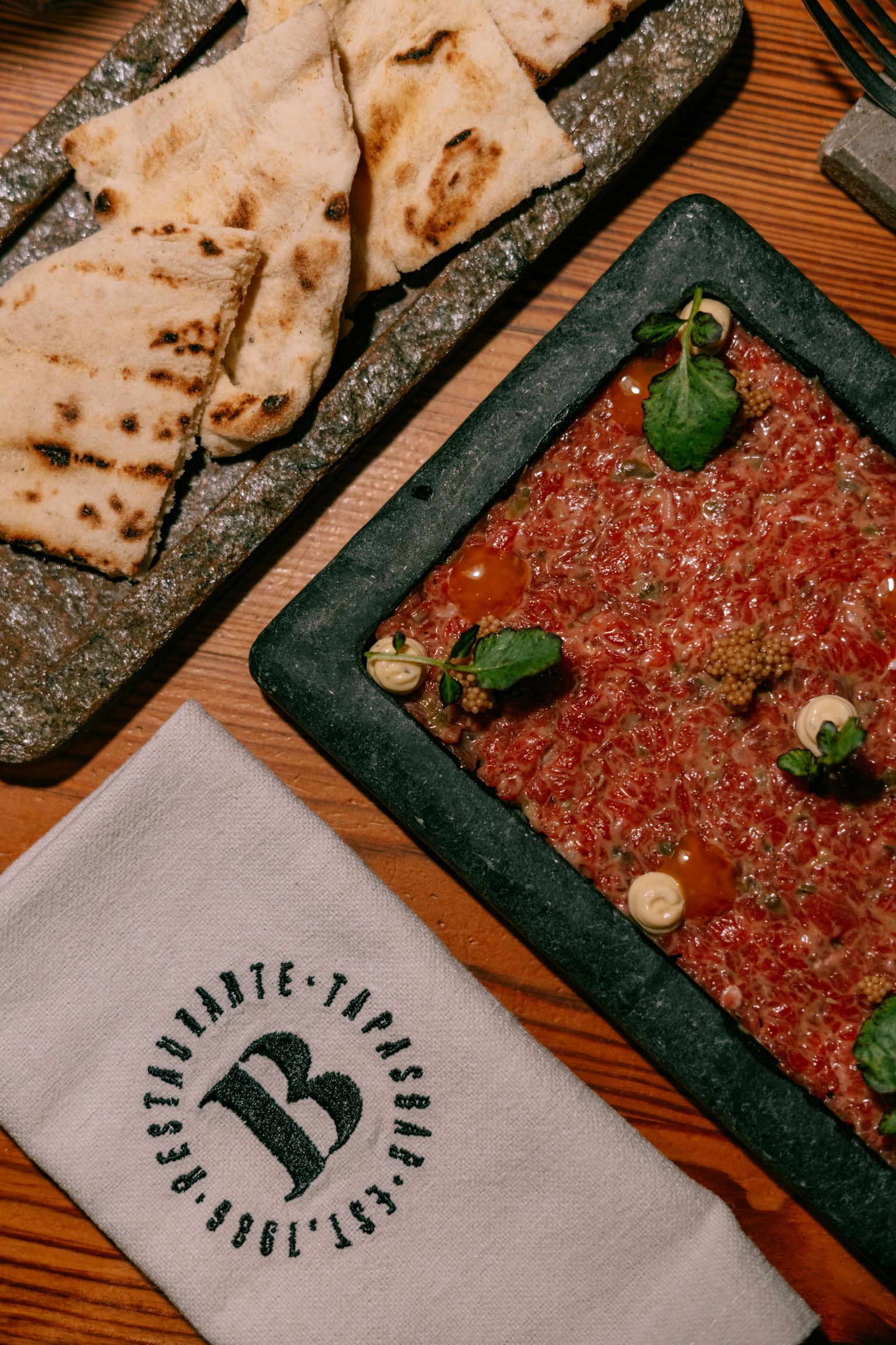 Steak tartar en una fuente de piedra con pan de pita tostado y servilleta de La Bodeguilla