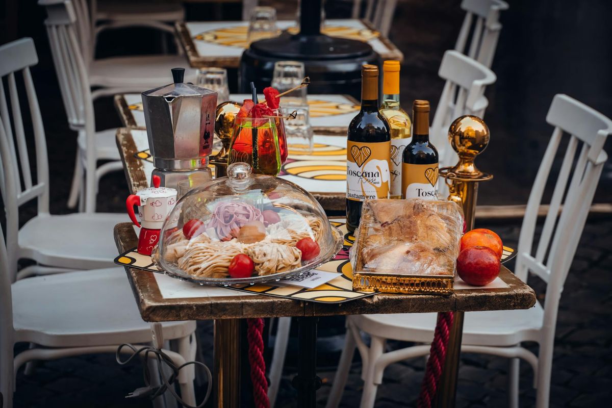 Close-up of a dining table set outdoors with Italian cuisine, featuring wine, coffee pot, and pastries.