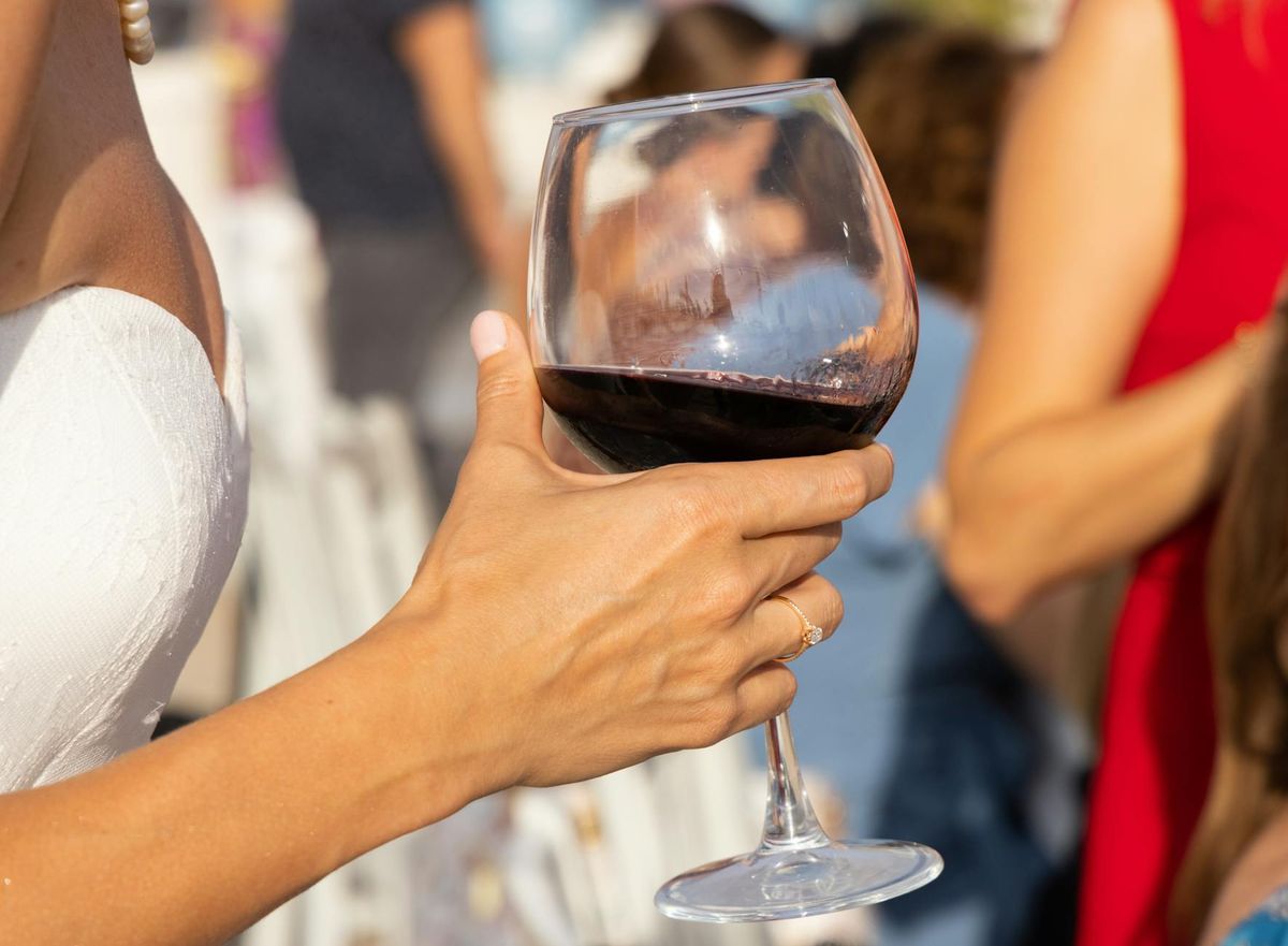Close-up of a hand holding a red wine glass at a wedding celebration.