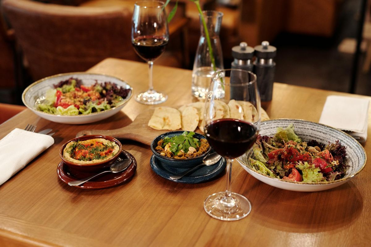 A beautifully arranged table featuring plates of Mediterranean food and glasses of red wine, set in a cozy restaurant atmosphere.