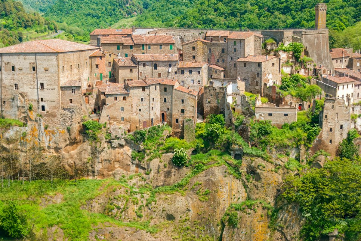 Scenic view of a historic Tuscan village nestled on a rocky cliff, surrounded by lush greenery.
