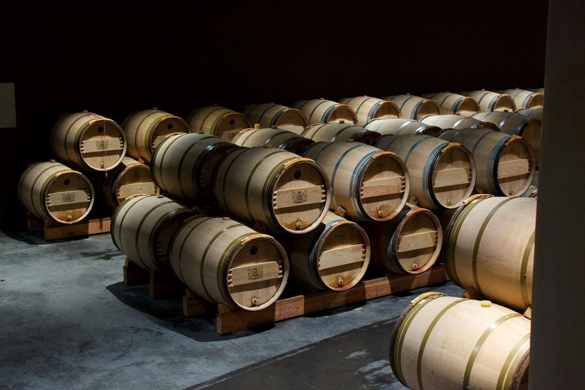 Stacked oak wine barrels in a dimly lit cellar in Pauillac, France.
