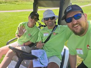 Three teammates in green Ronald McDonald House Charities volunteer shirts in a golf cart on the course, a tournament course map across one lap.