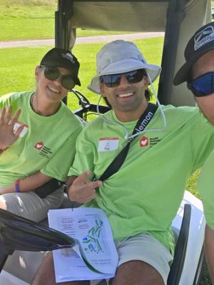 Three teammates in green Ronald McDonald House Charities volunteer shirts in a golf cart on the course, a tournament course map across one lap.