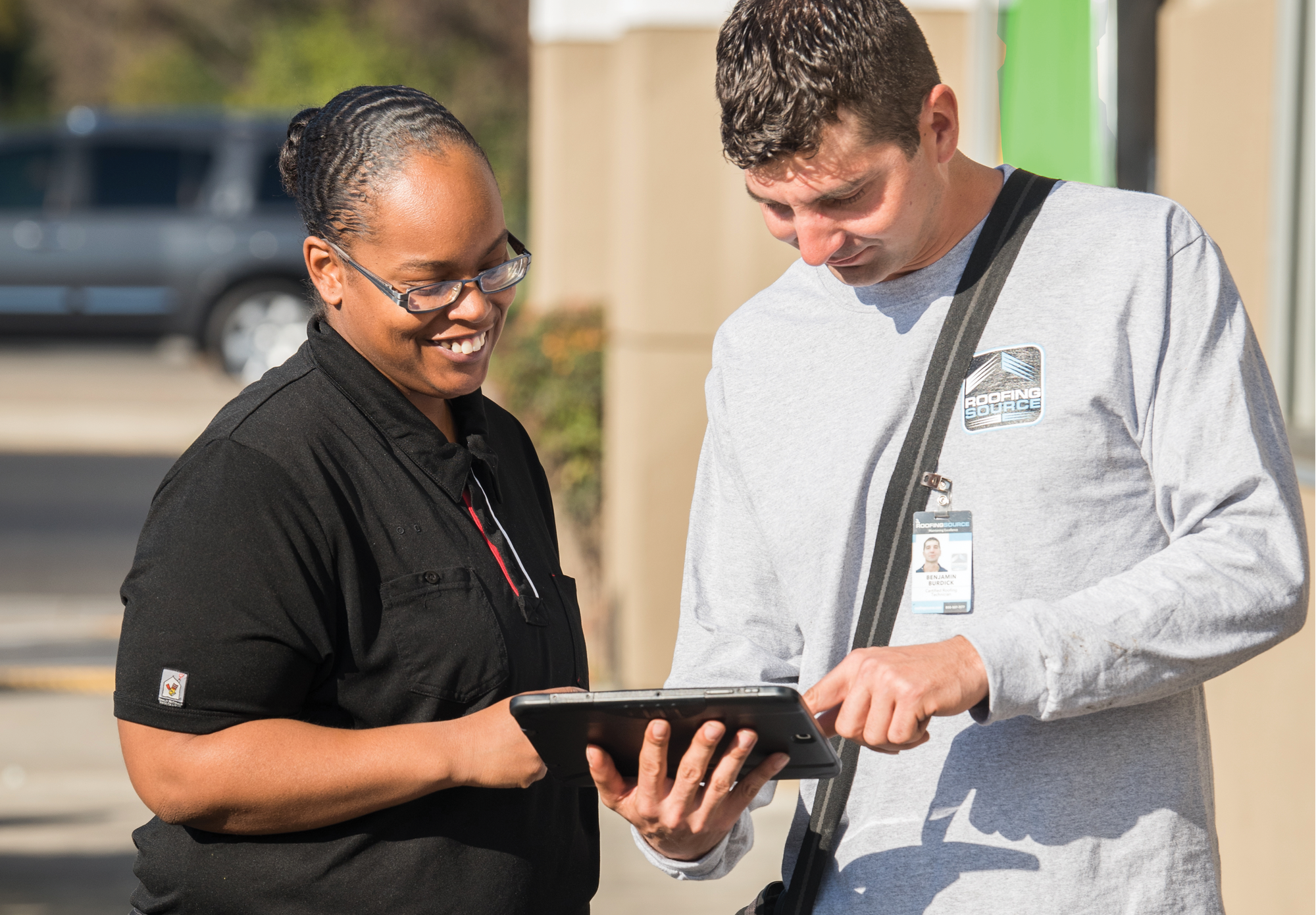 A RoofingSource teammate showing a tablet screen to a person in restaurant uniform outside a store