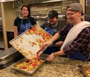 Three RoofingSource volunteers in aprons serving a meal in a Ronald McDonald House kitchen