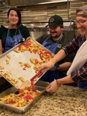 Three RoofingSource volunteers in aprons serving a meal in a Ronald McDonald House kitchen