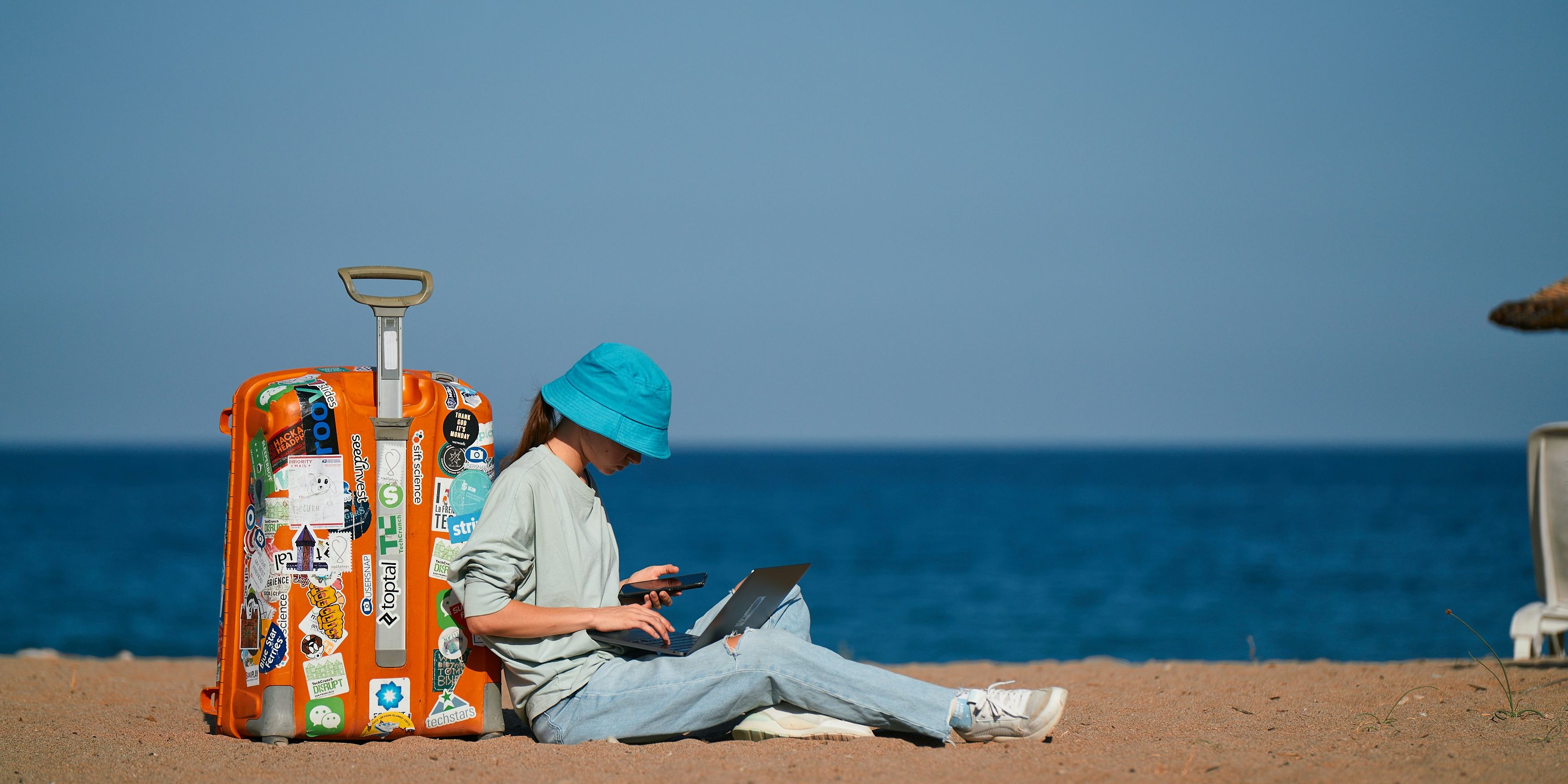 a woman is sitting on the beach with a suitcase and a laptop .