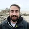a man with a beard is standing on a rocky beach .