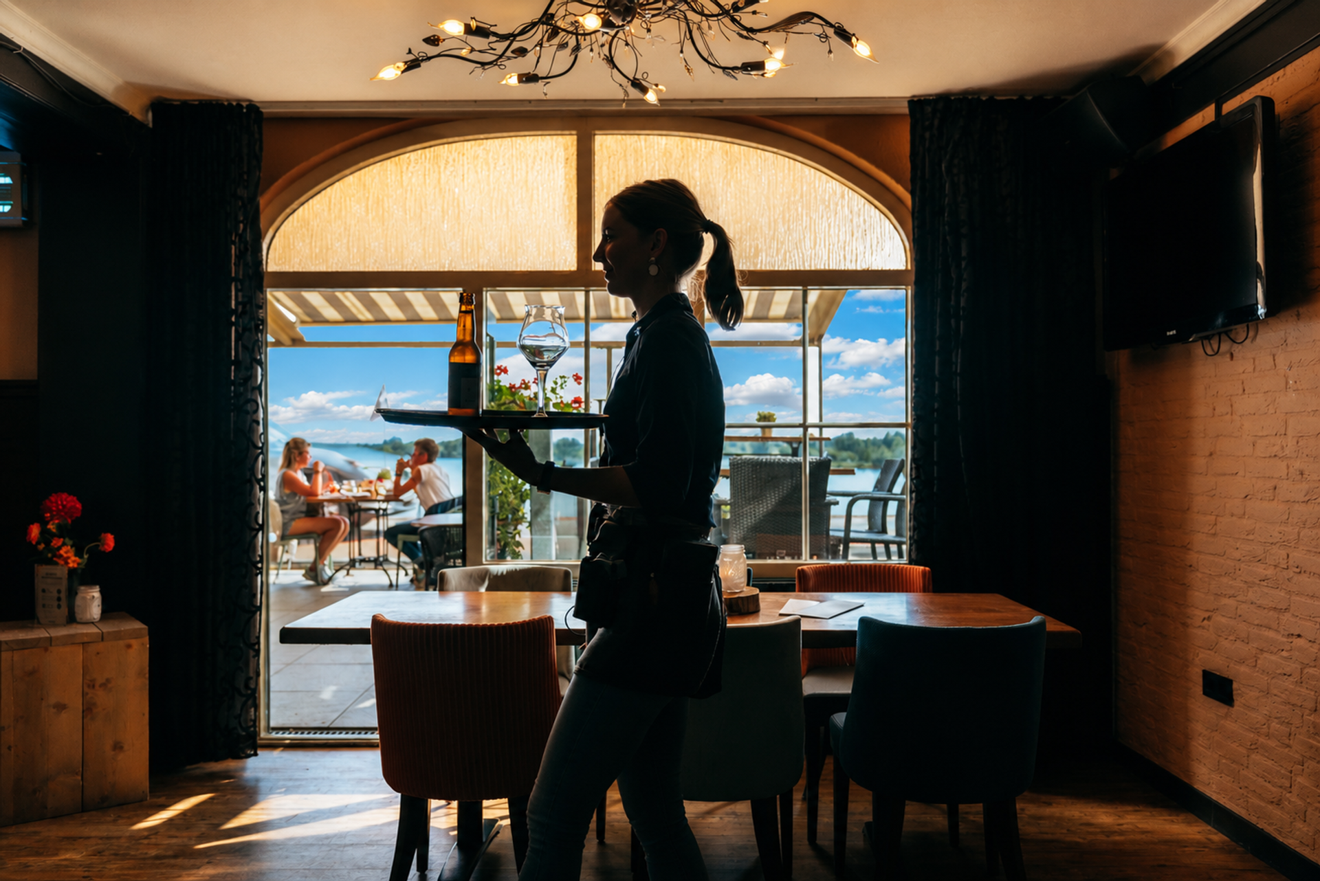 Medewerker bediening met dienblad, gasten op het terras van Hotel Hoogeerd
