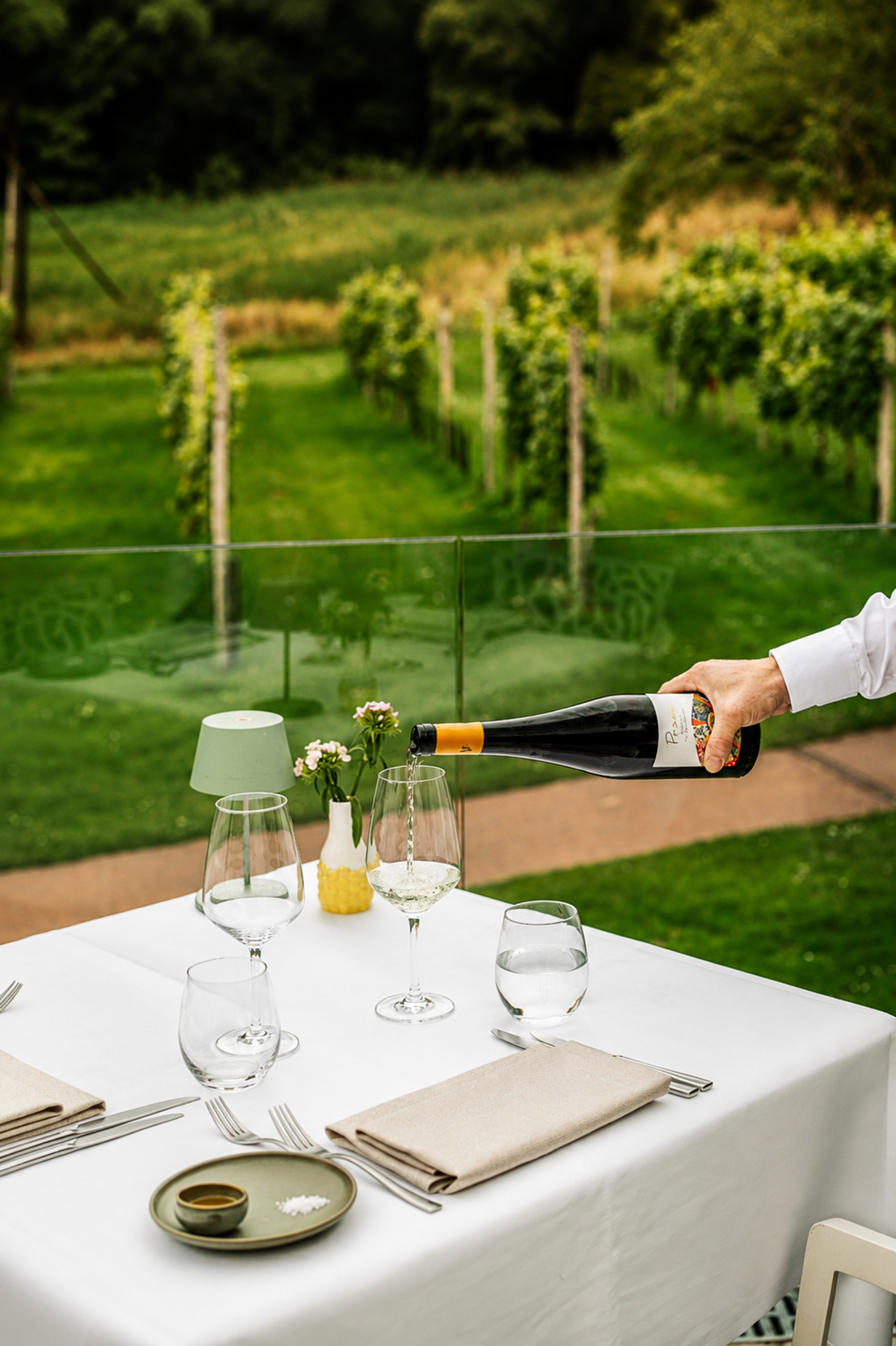 Een glas wijn wordt ingeschonken aan een gedekte tafel met uitzicht op de wijngaard van Hotel Winselerhof