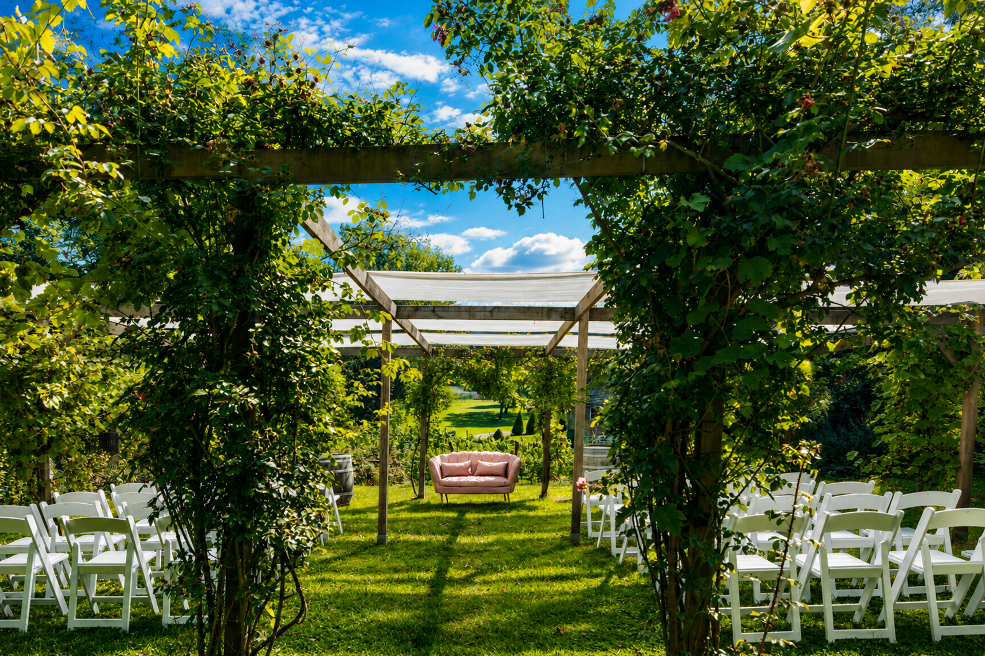 Romantische trouwlocatie in de tuin van Landgoed Winselerhof met begroeide pergola, witte stoelen en roze bank