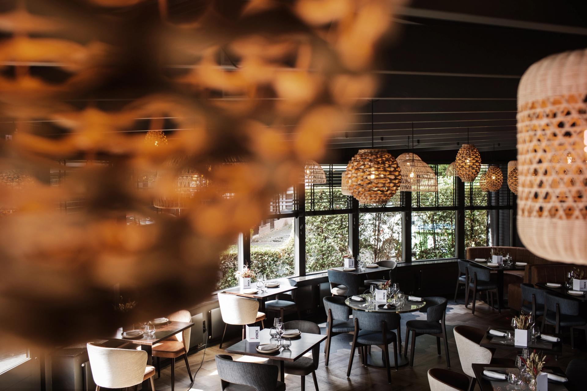 Interieur van Restaurant Vonck in Hotel Paping in Ommen met ronde tafels, blauwe stoelen, rieten hanglampen en groot kunstwerk