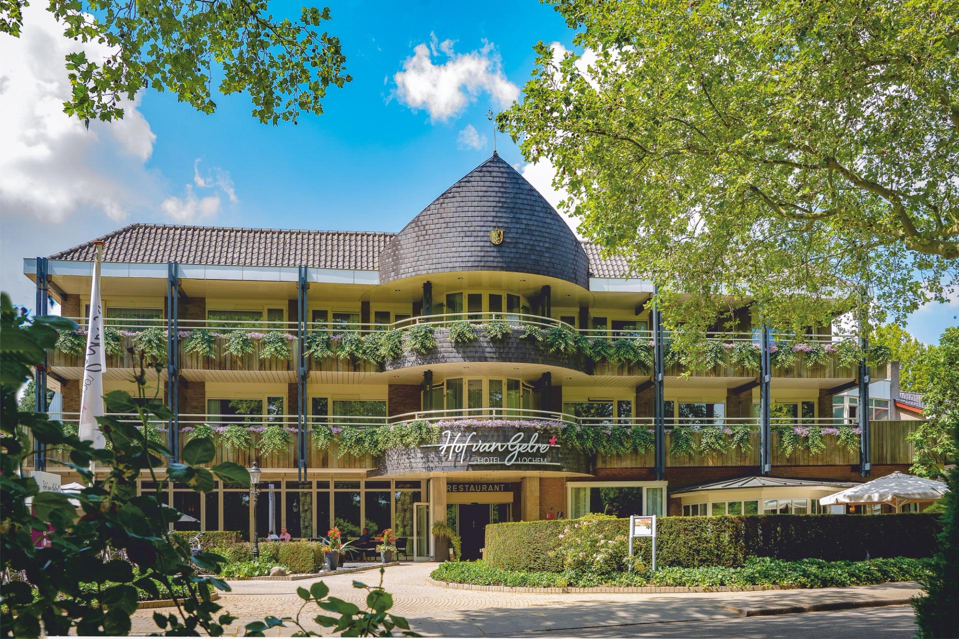 Karakteristieke gevel van Hotel Hof van Gelre in Lochem met begroeide balkons en torenspits verscholen in het groen