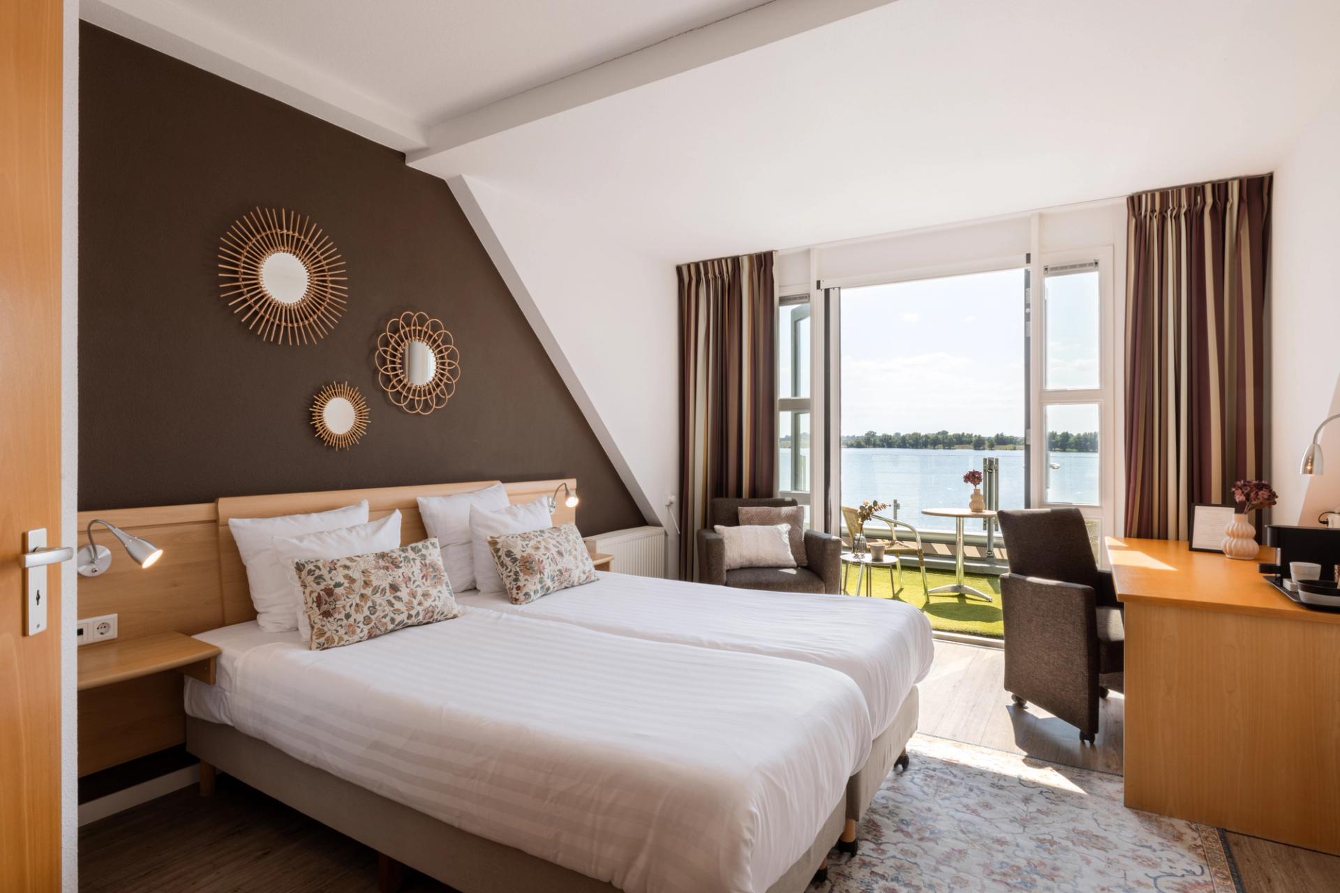 Hotelkamer met tweepersoonsbed, zithoek en panoramisch uitzicht op de Maas bij Hotel Restaurant Hoogeerd in Niftrik
