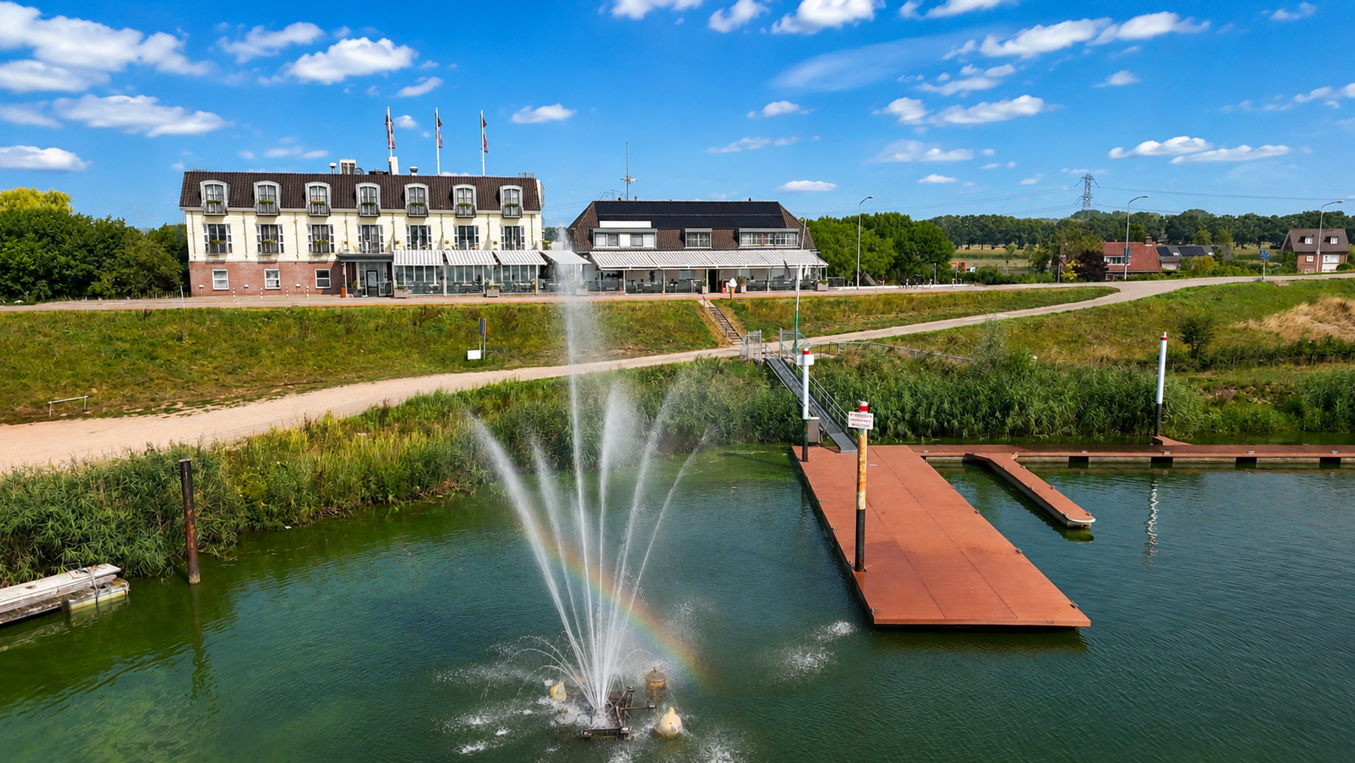 Hotel & Restaurant Hoogeerd aan de Maas met fontein, regenboog, terras en aanlegsteiger in de natuur