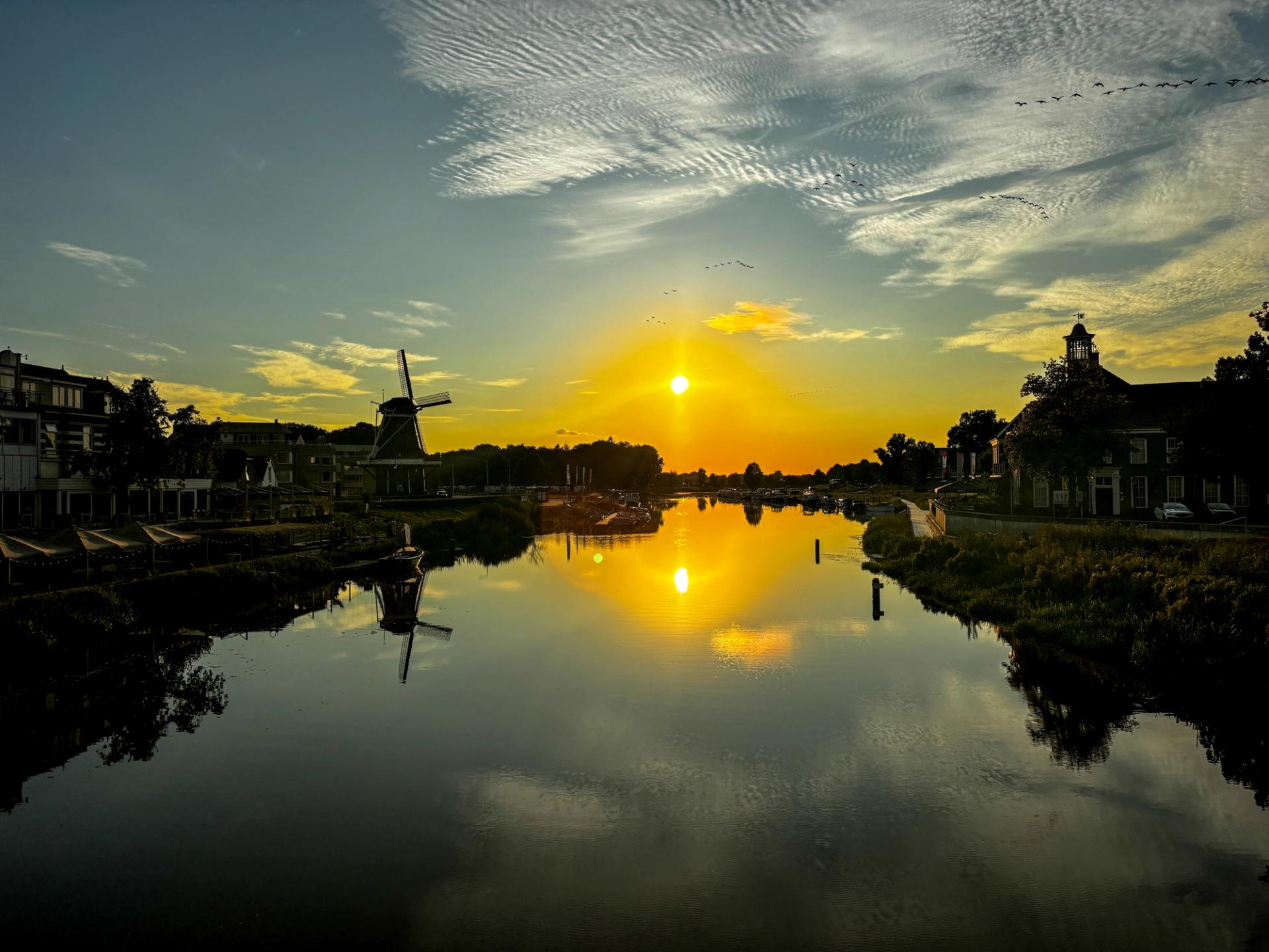 Zonsondergang boven de Vecht in Ommen met molen als silhouet en gouden weerspiegeling in het water. Hotel de Zon & Brasserie Bresson