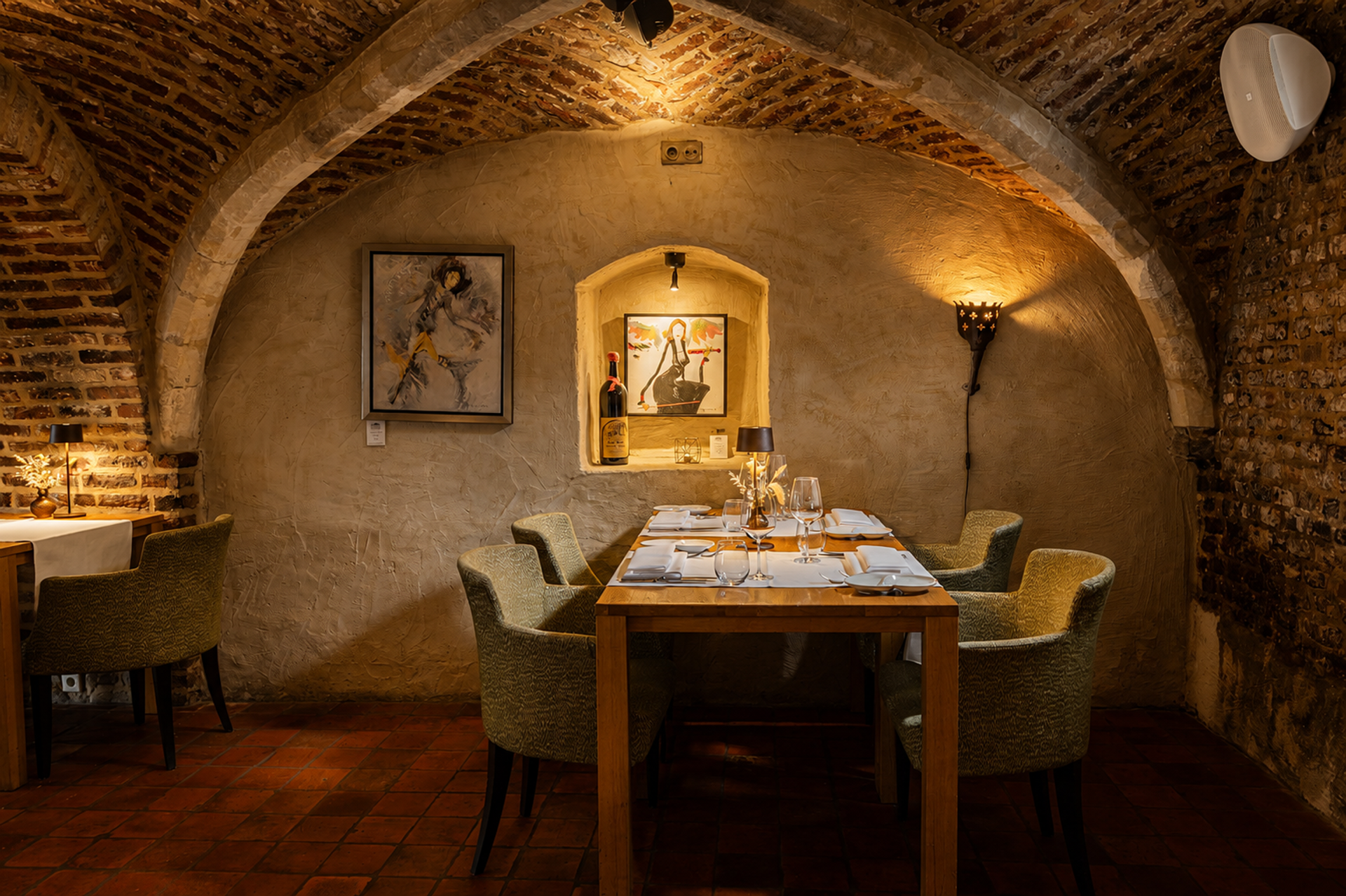 Gedekte tafels onder bakstenen gewelven in restaurant Luigi's in Winselerhof, met kunstwerken, wijnnis en terracotta vloer