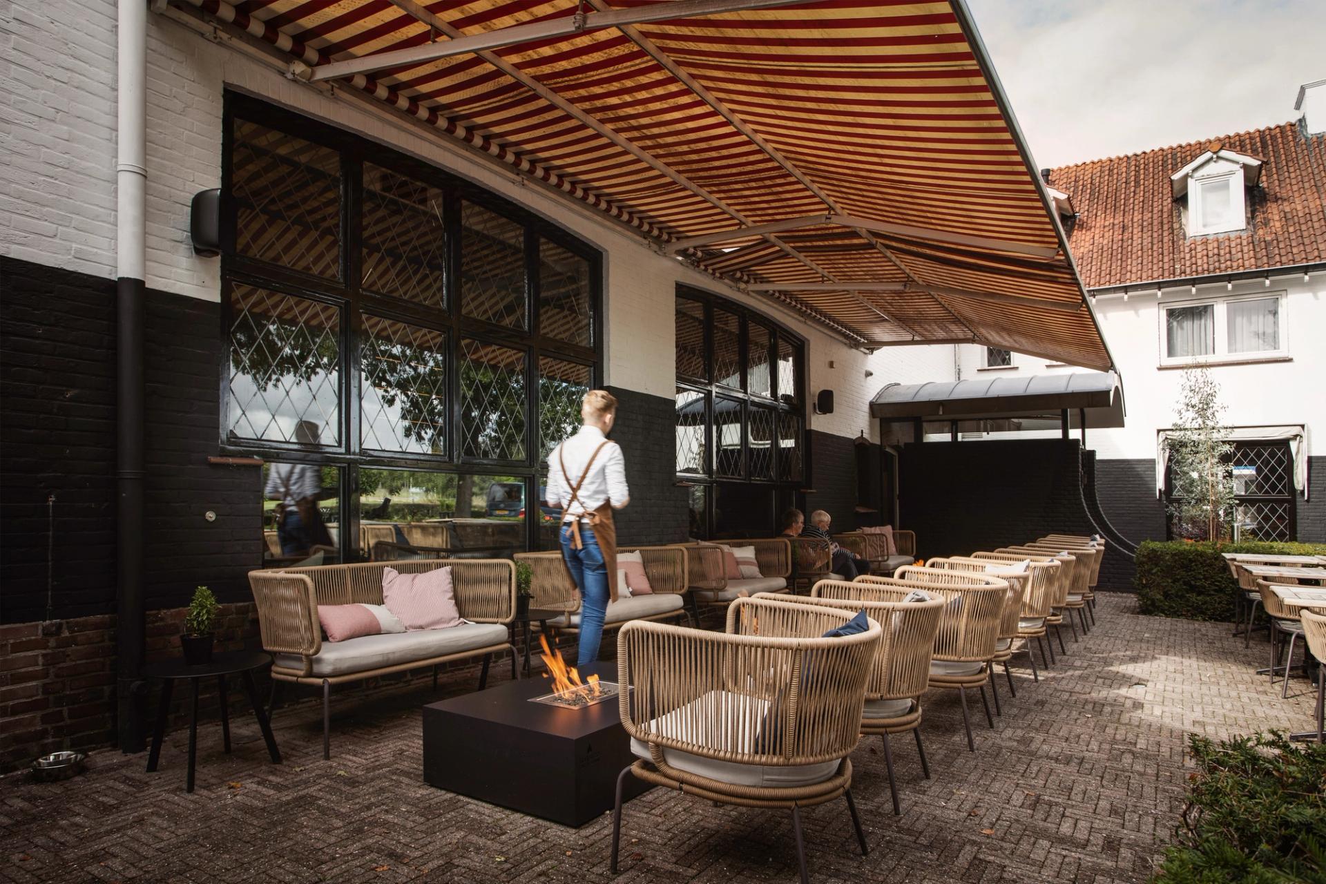 Terras van Hotel Paping en Restaurant Vonck in Ommen met rieten loungestoelen, vuurkorf en gestreepte luifel