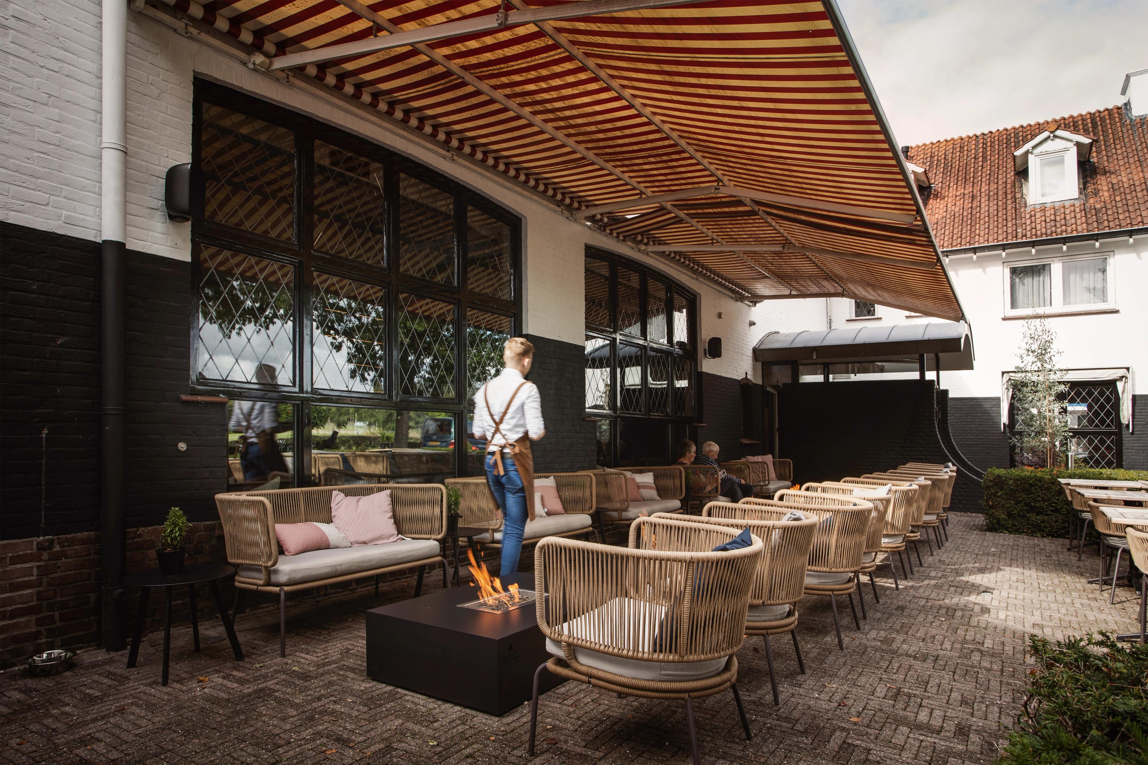 Terras van Hotel Paping en Restaurant Vonck in Ommen met rieten loungestoelen, vuurkorf en gestreepte luifel