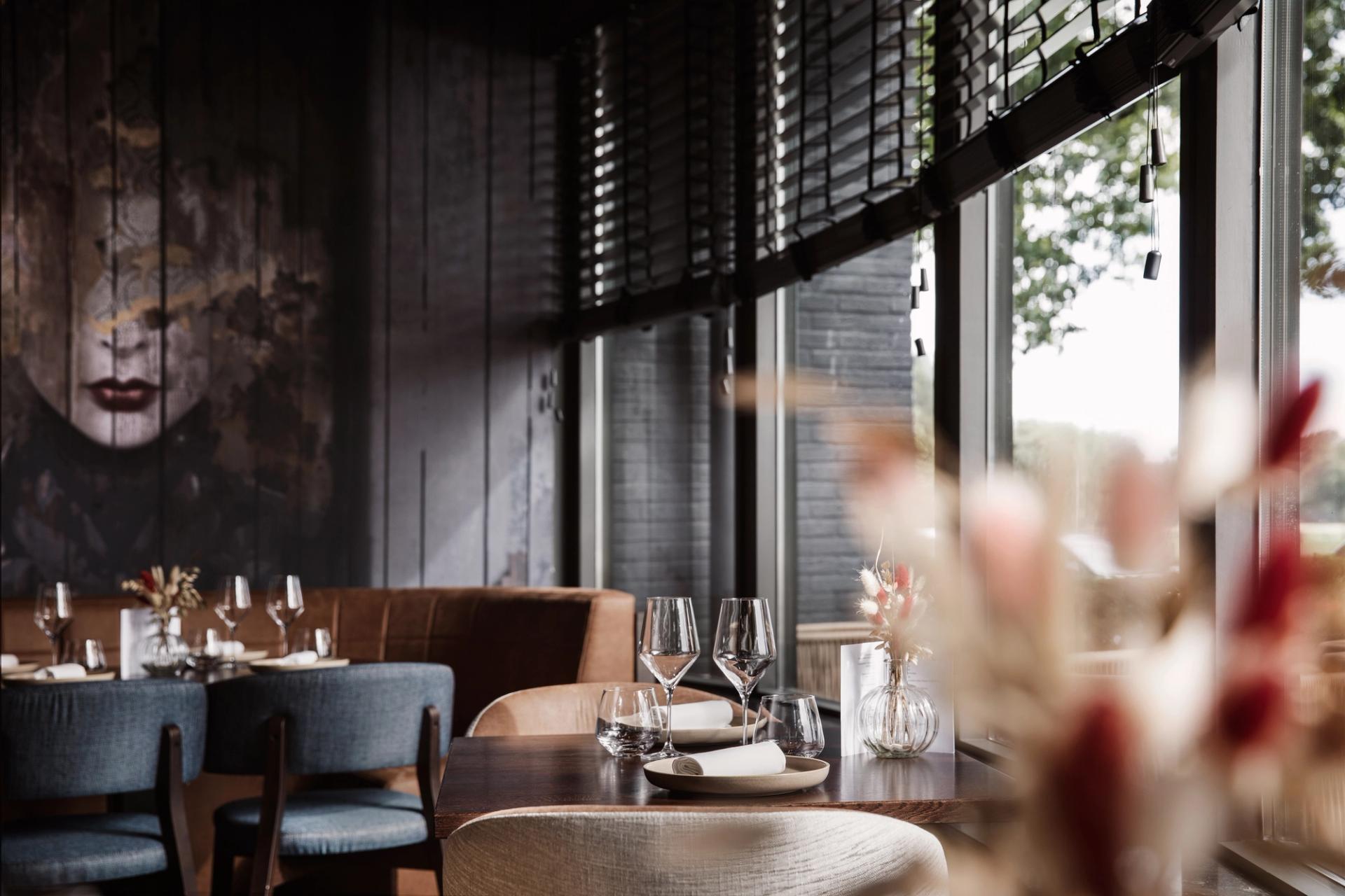 Interieur van Restaurant Vonck in Hotel Paping in Ommen met ronde tafels, blauwe stoelen, rieten hanglampen en groot kunstwerk