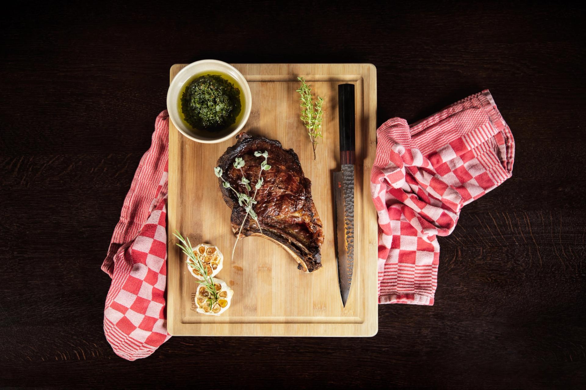 Gegrilde côte de boeuf op een houten snijplank met chimichurri, geroosterde knoflook en tijm — Restaurant Vonck, Hotel Paping in Ommen