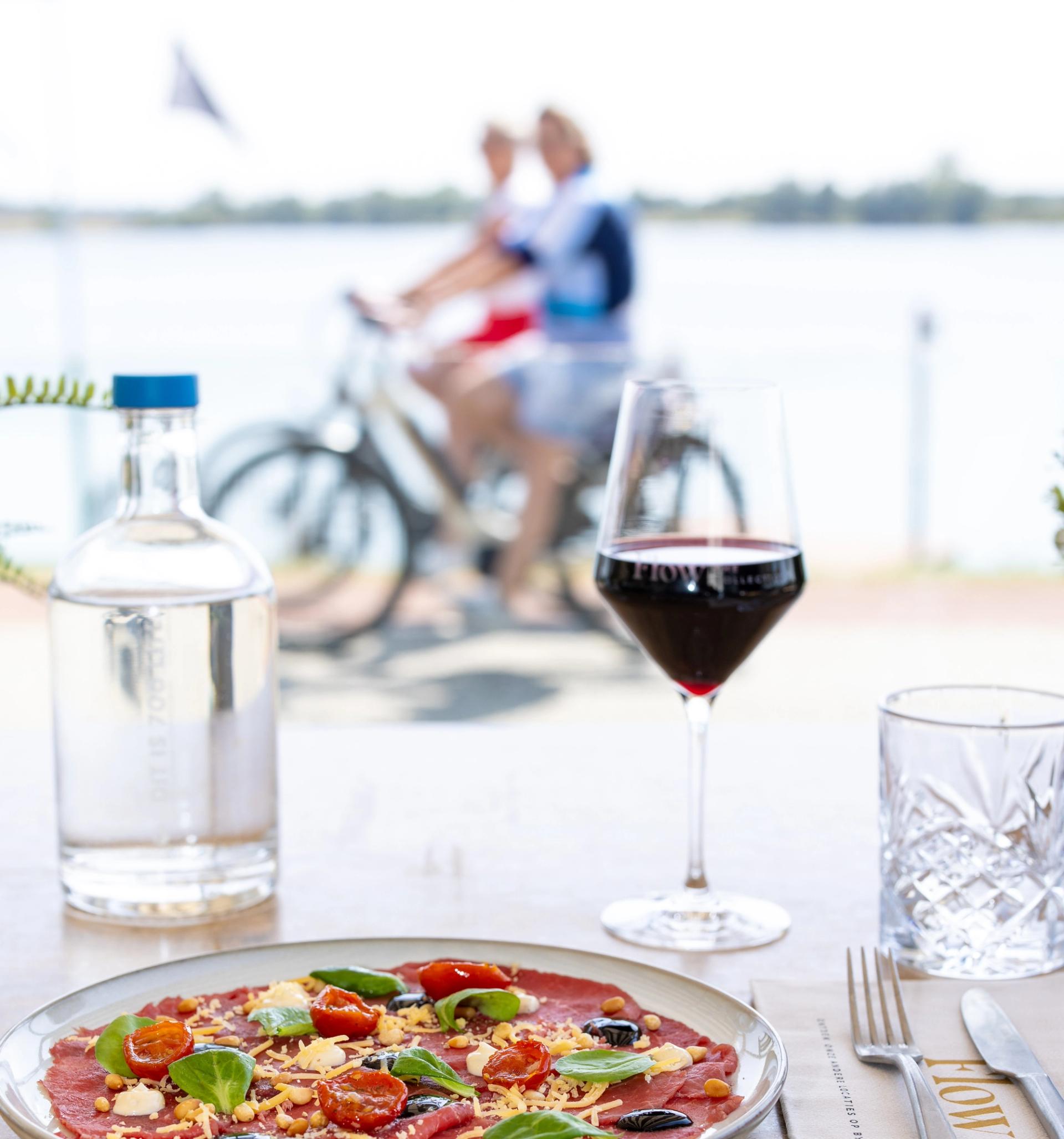 Radfahrer auf einem Deich zwischen weiten Poldern im Land van Maas en Waal, mit Obstgärten am Weg