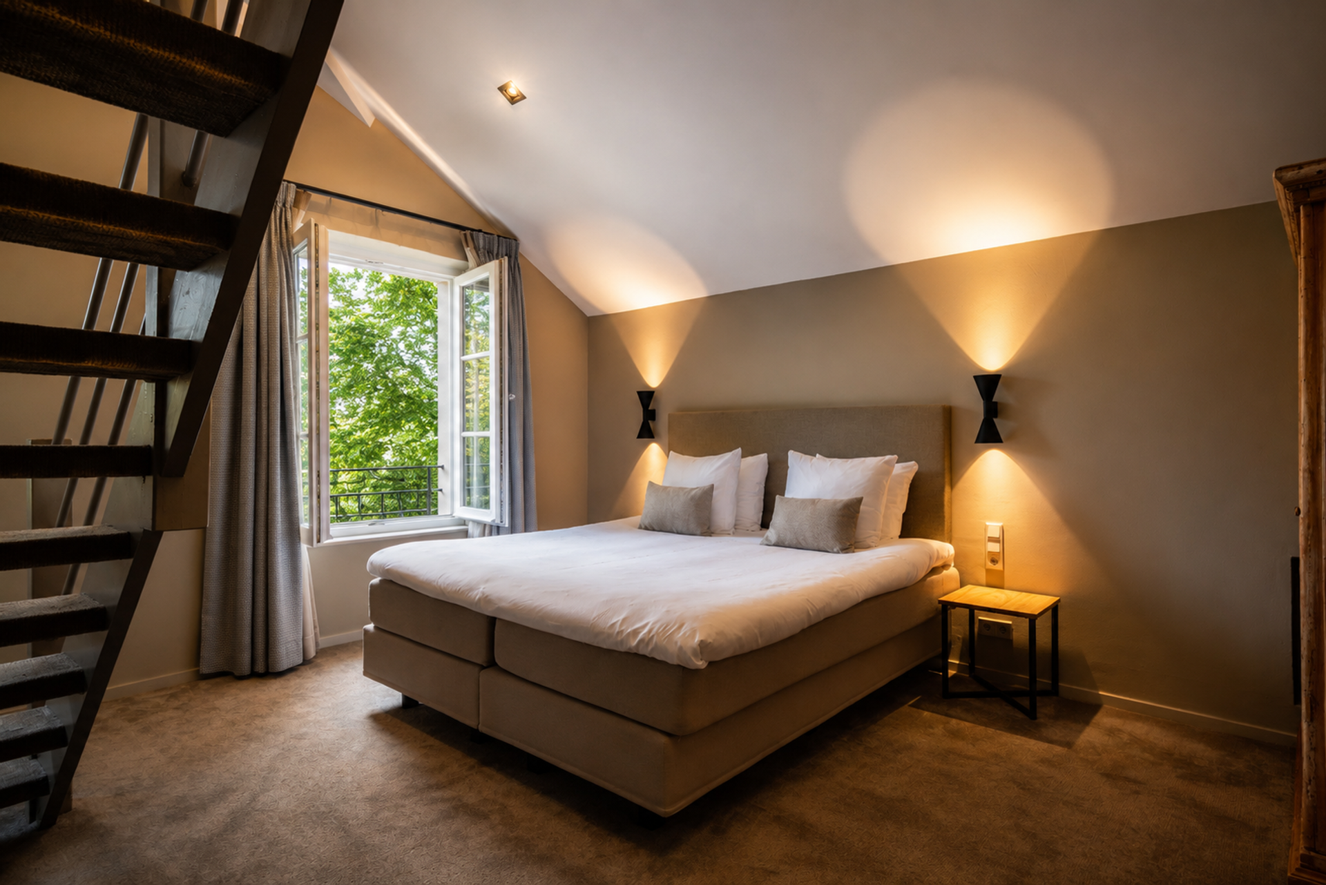 Sfeervolle hotelkamer met tweepersoonsbed, open raam met uitzicht op het groen en authentieke trap bij Landgoed Winselerhof in Zuid-Limburg