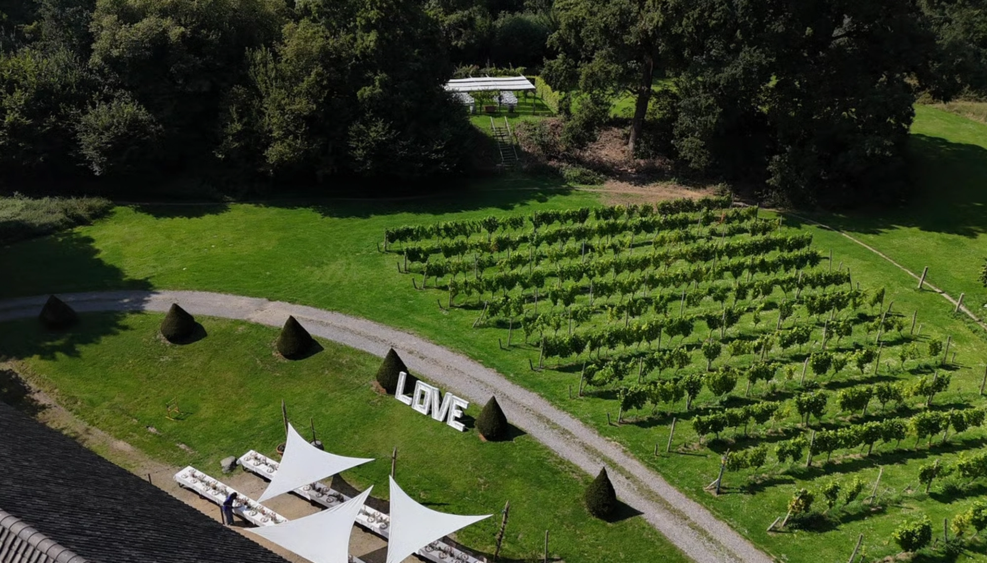Bruiloftsdiner bij Winselerhof in Limburg met lange gedekte tafels, elegante tafeldecoratie, bloemen, kaarsen en sfeerverlichting onder schaduwdoeken in een groene tuinsetting.