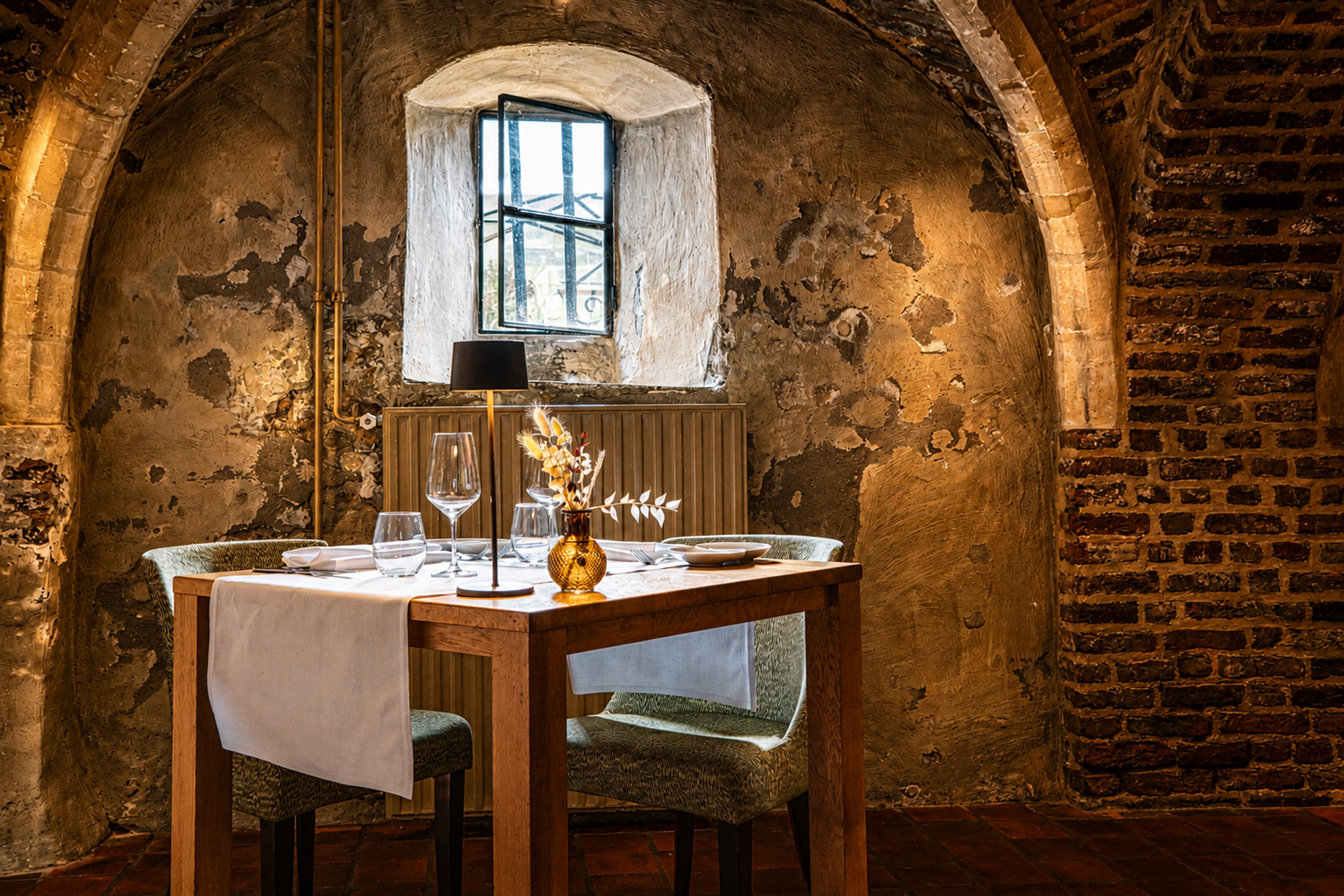 Intiem gedekte tafel in het historische gewelfde restaurant Luigi's in Winselerhof, met bakstenen bogen en een gouden tafellamp