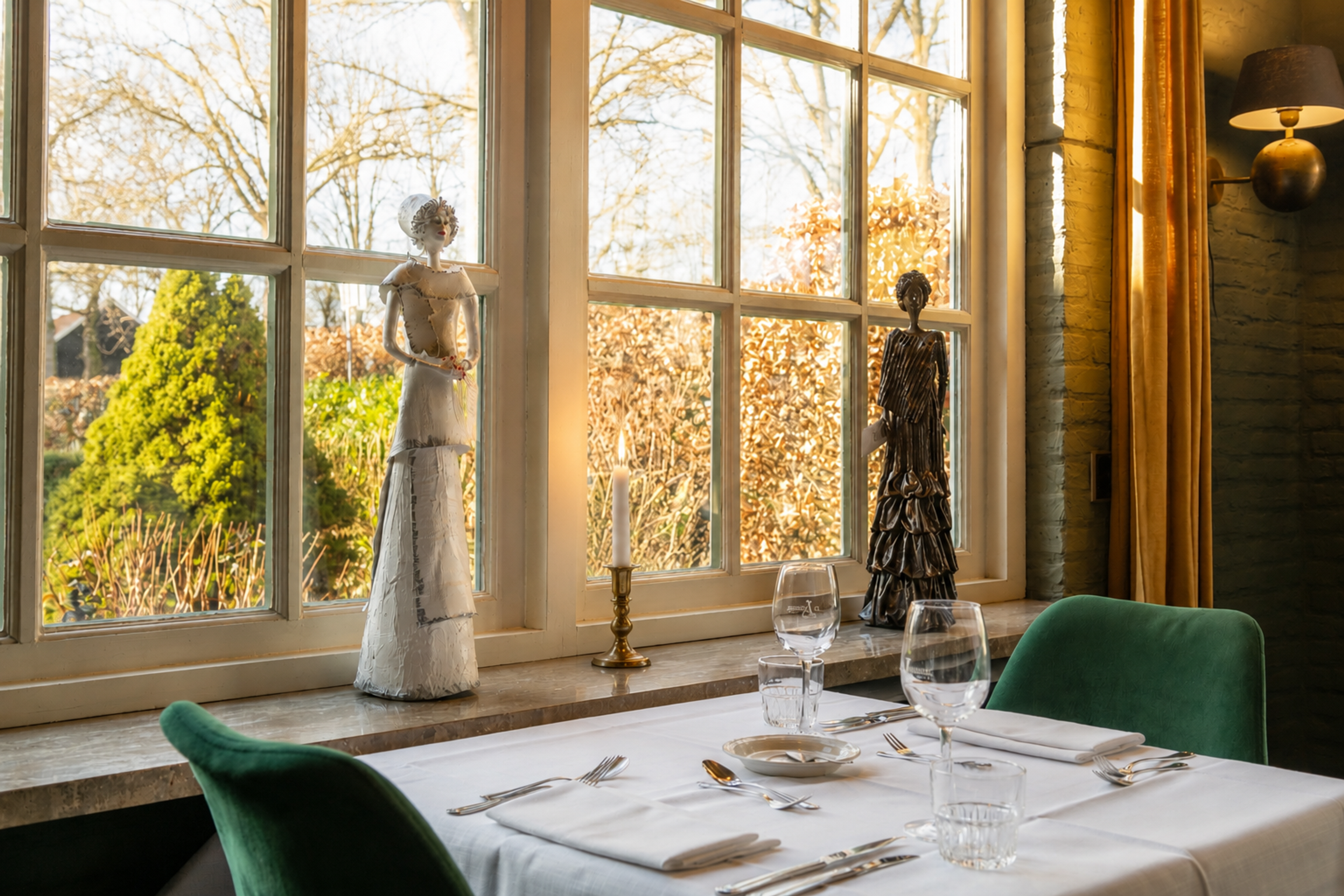 Sfeervolle restauranttafel met kunstbeelden, kaarslicht en uitzicht op de natuur bij Hotel de Landmarke in Ootmarsum