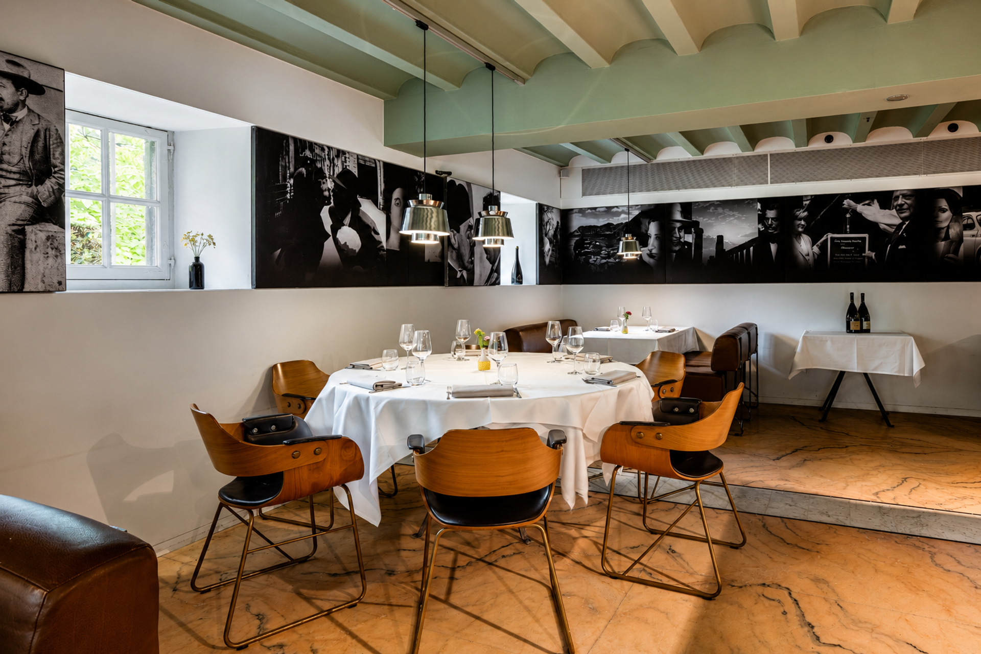 Interior of restaurant Pirandello at Winselerhof with round tables, wooden chairs and black-and-white photo wall of Italian cinema icons