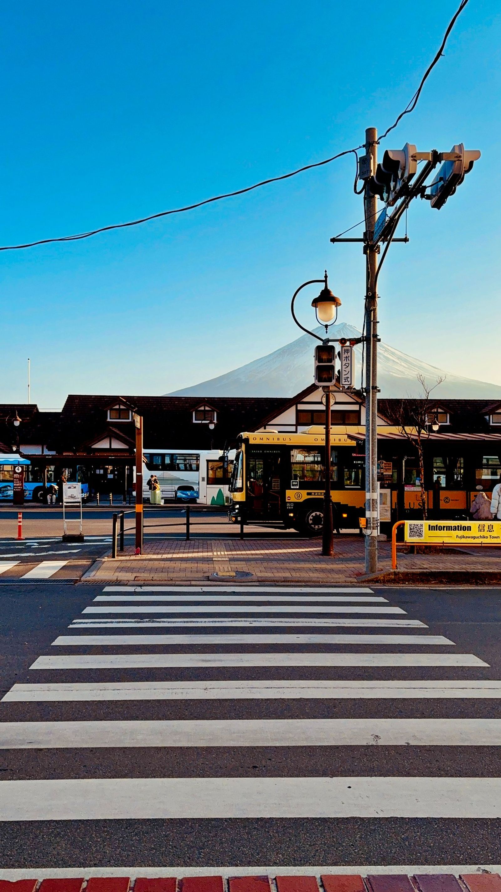 A pedestrian crossing below Mount Fuji, buses waiting at the station